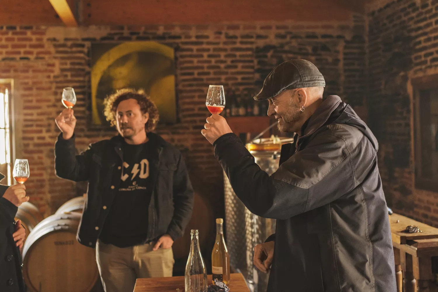 Two men in a wine cellar carefully inspecting the clarity and color of wine in glasses.