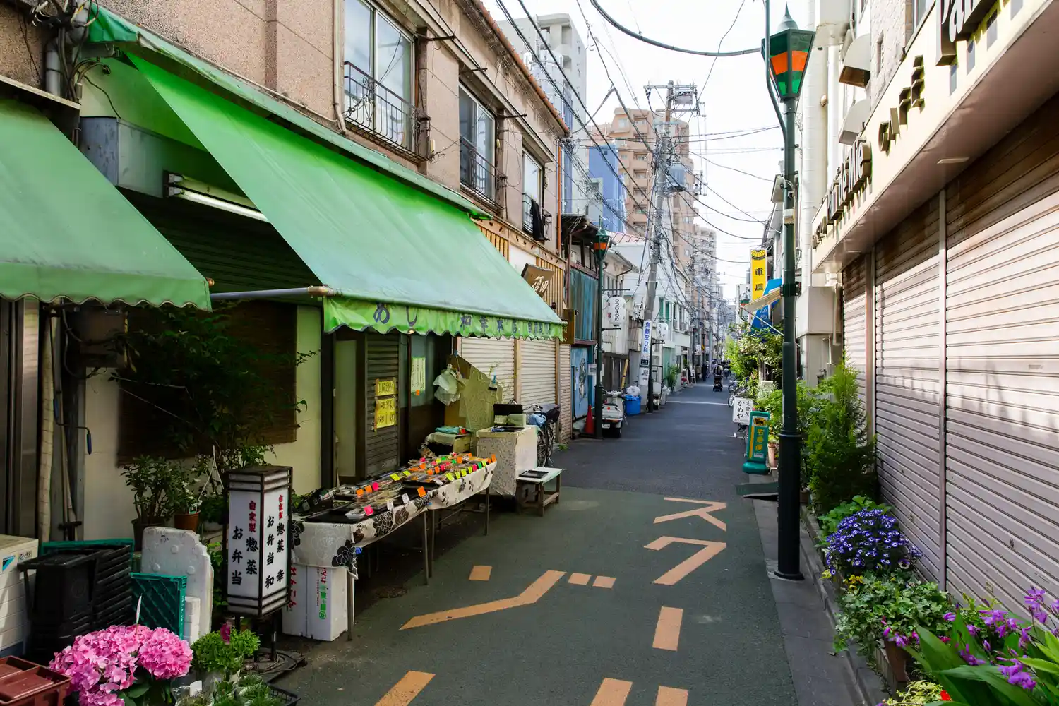 A narrow, quiet residential street in Tokyo's Yanaka neighborhood with local shops and potted plants.