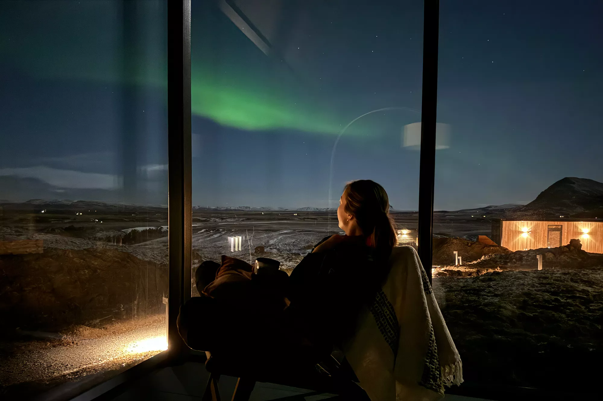Green Northern Lights dancing in the sky above a mirror glass cabin in Iceland.