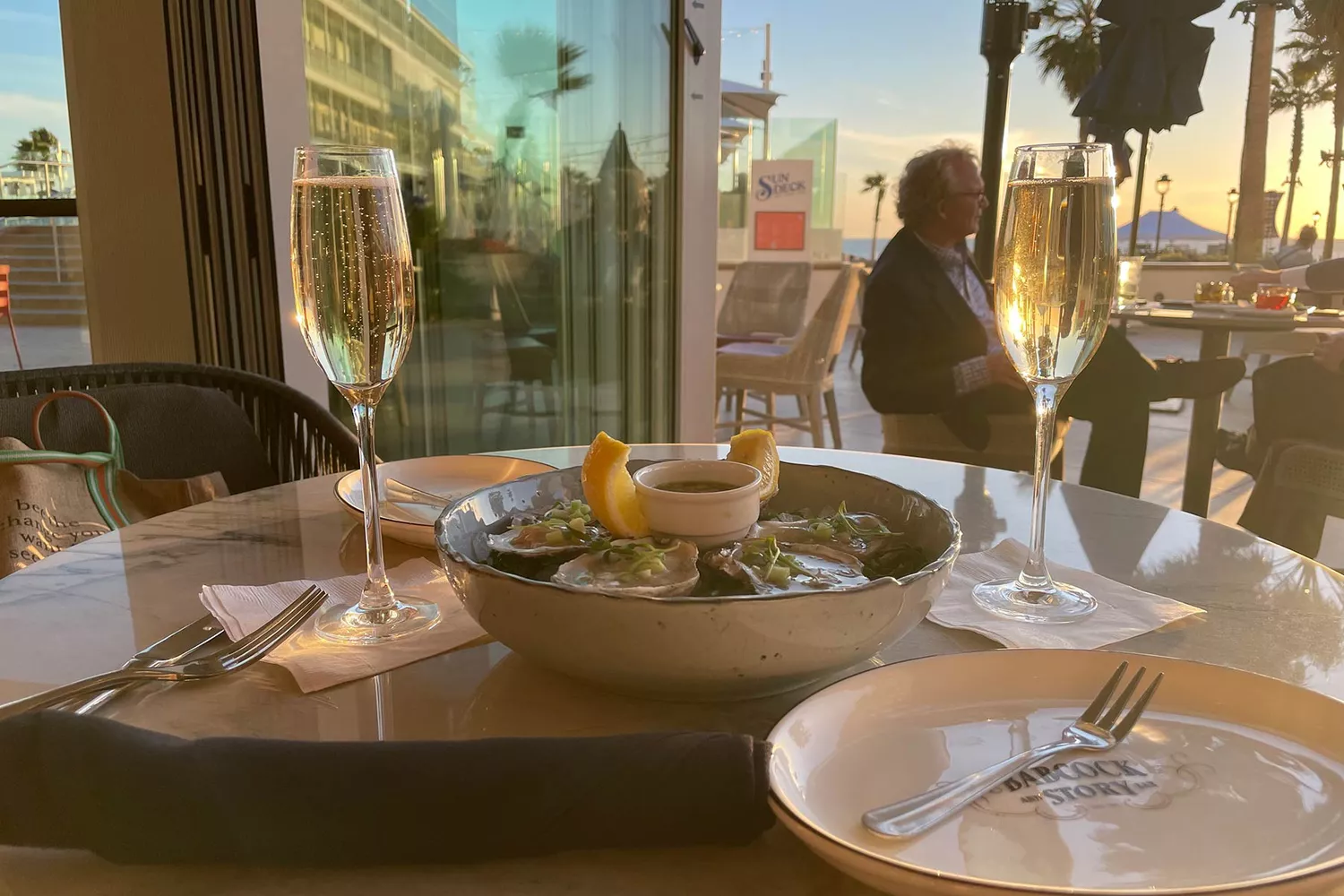 Two glasses of champagne and a plate of oysters on a sun-drenched deck.