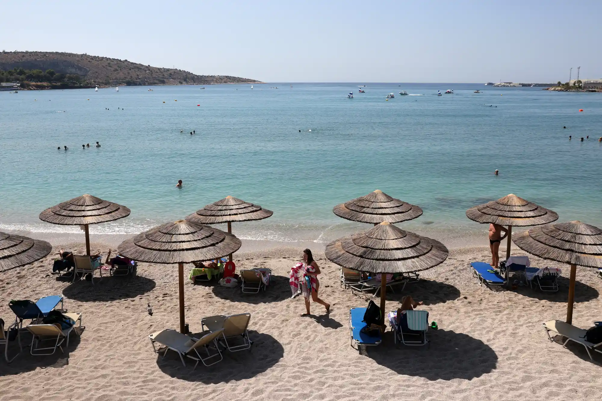 Beach umbrellas and sun loungers on a pristine sandy shore along the Saronic Gulf with clear turquoise water.