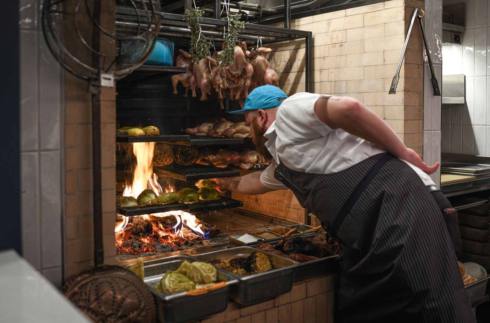 A chef cooking over an open fire hearth in a professional kitchen.
