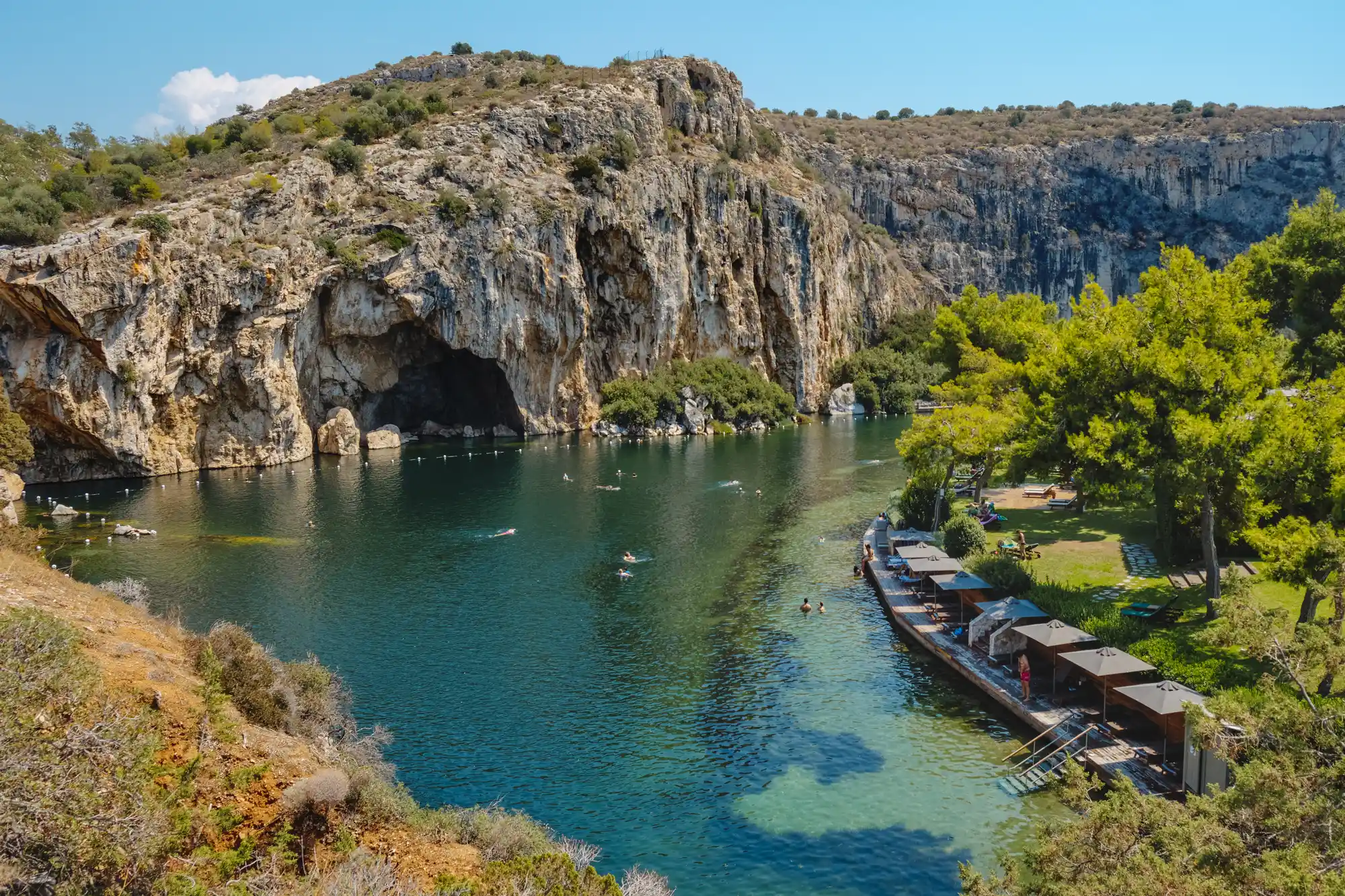 A serene view of Lake Vouliagmeni's emerald waters situated at the base of towering limestone cliffs.