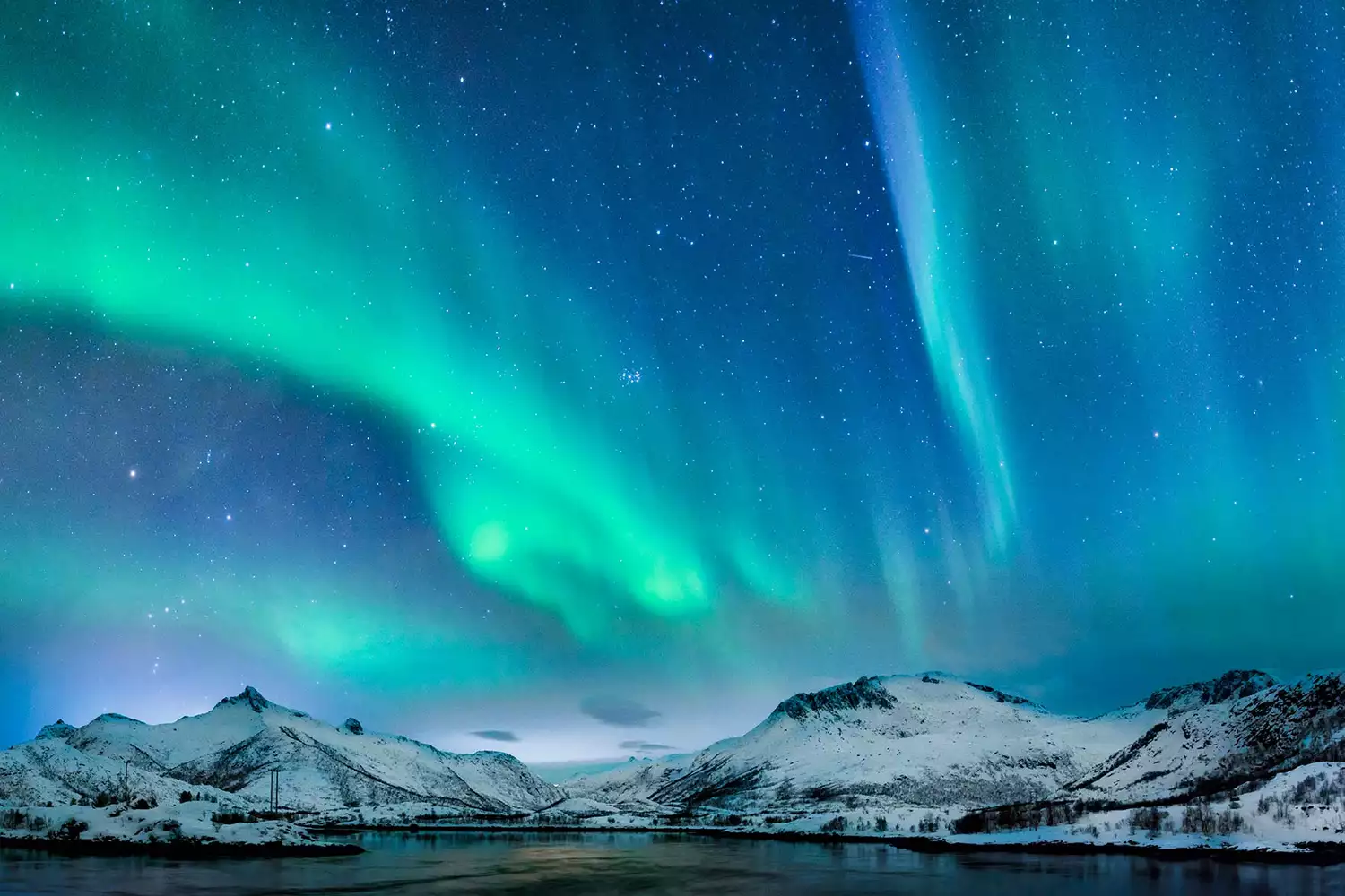 Bright green aurora borealis dancing over the mountains and ocean in the Lofoten Islands.