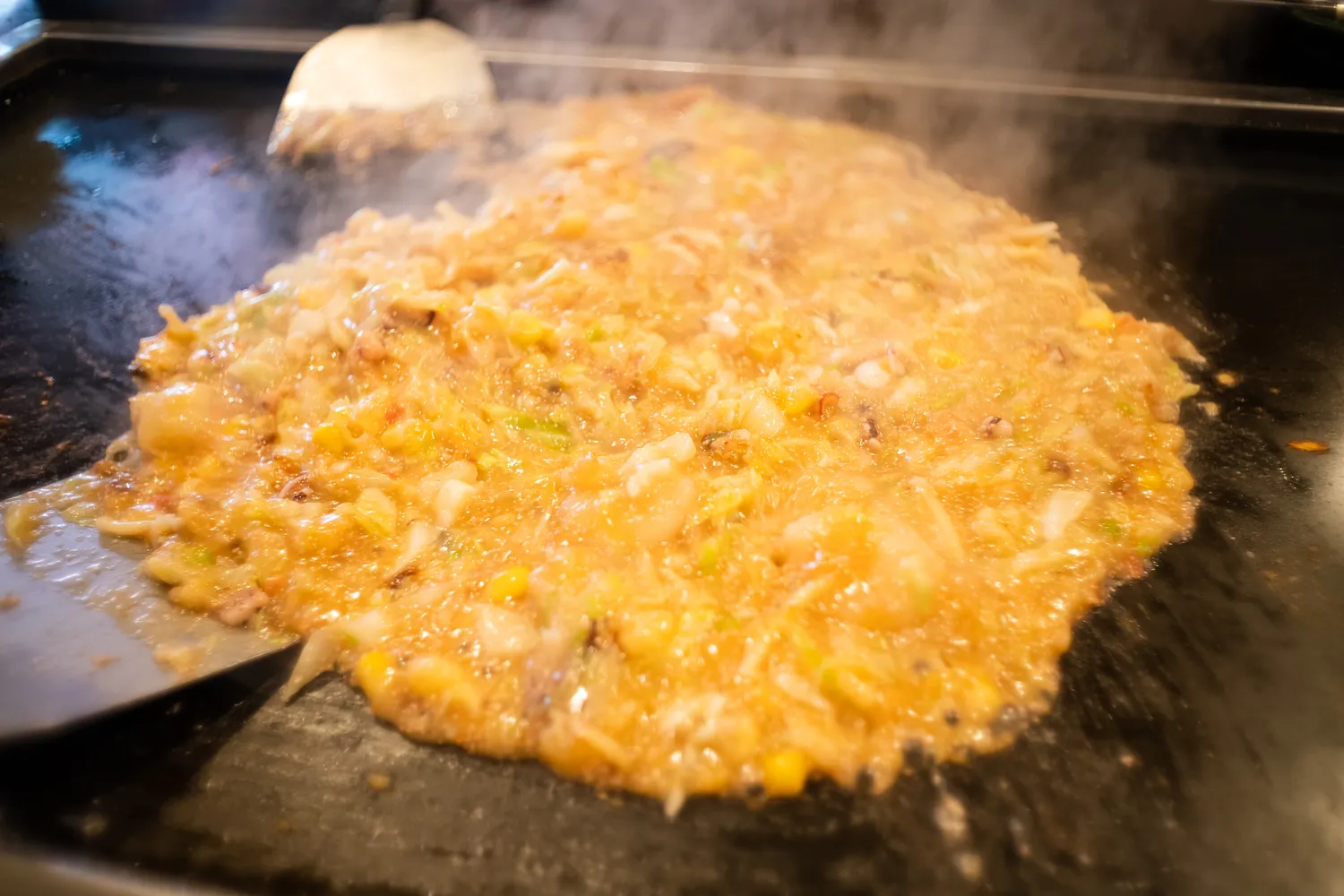 Monjayaki being cooked with spatulas on a traditional tabletop iron griddle.
