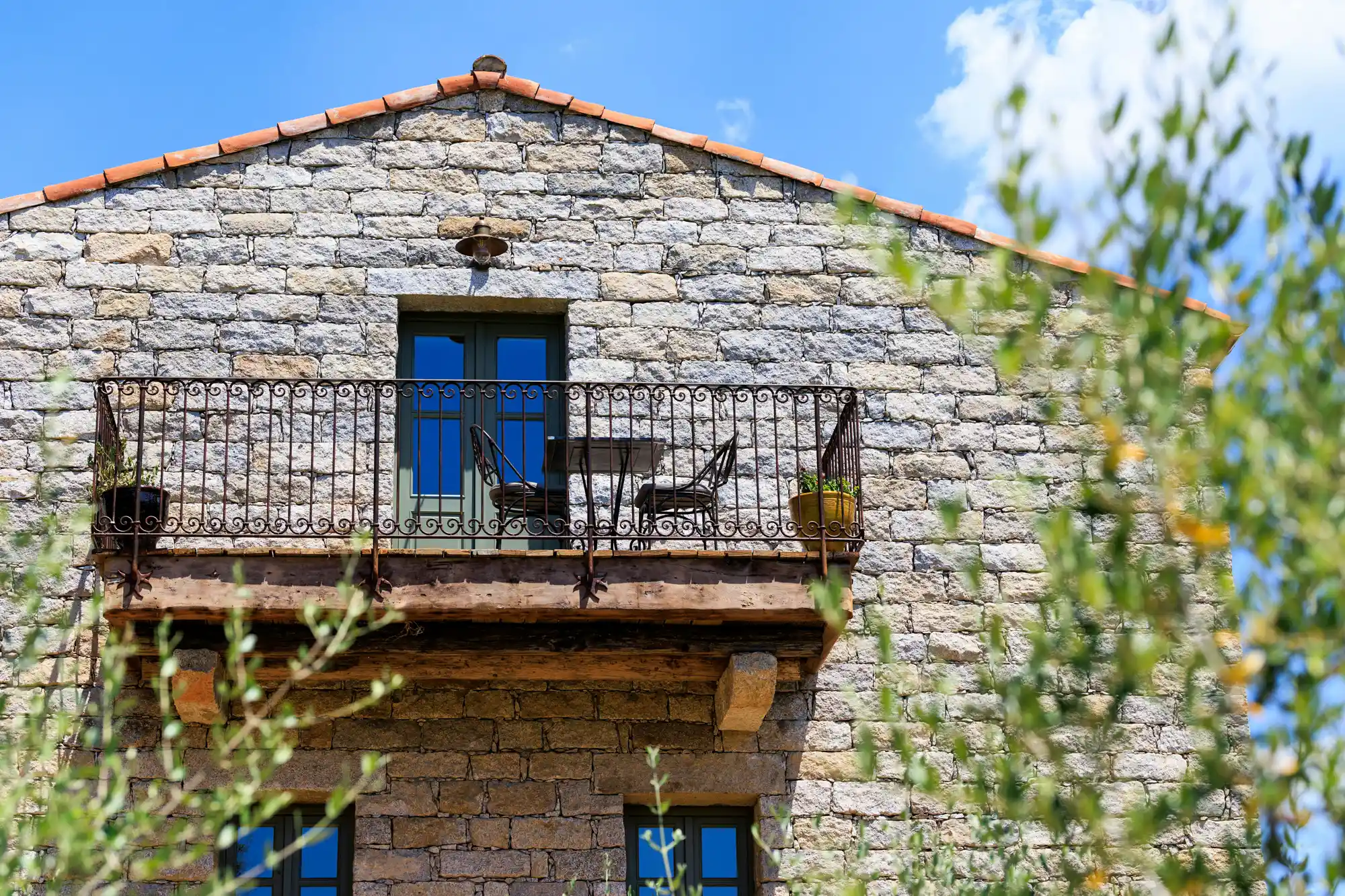 A stone balcony with outdoor seating overlooking dense green foliage under a clear sky.