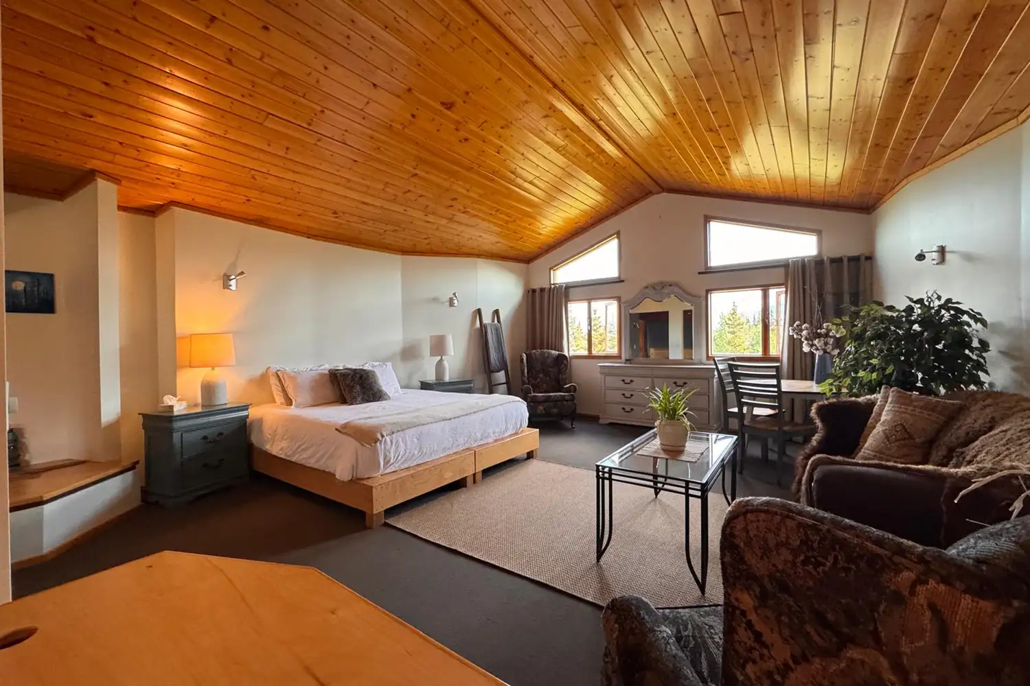 The interior of a warm, wooden lodge guest room with a large window showing the snowy landscape outside.