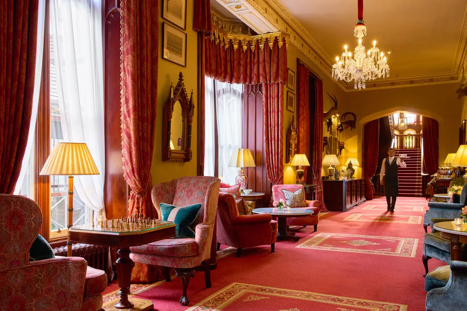 A grand gallery hallway in Dromoland Castle featuring red carpets, ornate furniture, and crystal chandeliers.