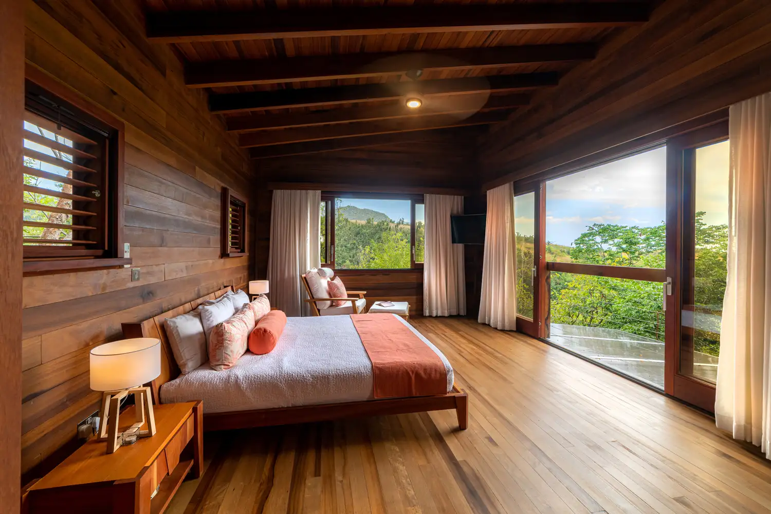 Interior of a modern wooden villa at Secret Bay with large windows looking out onto tropical greenery.