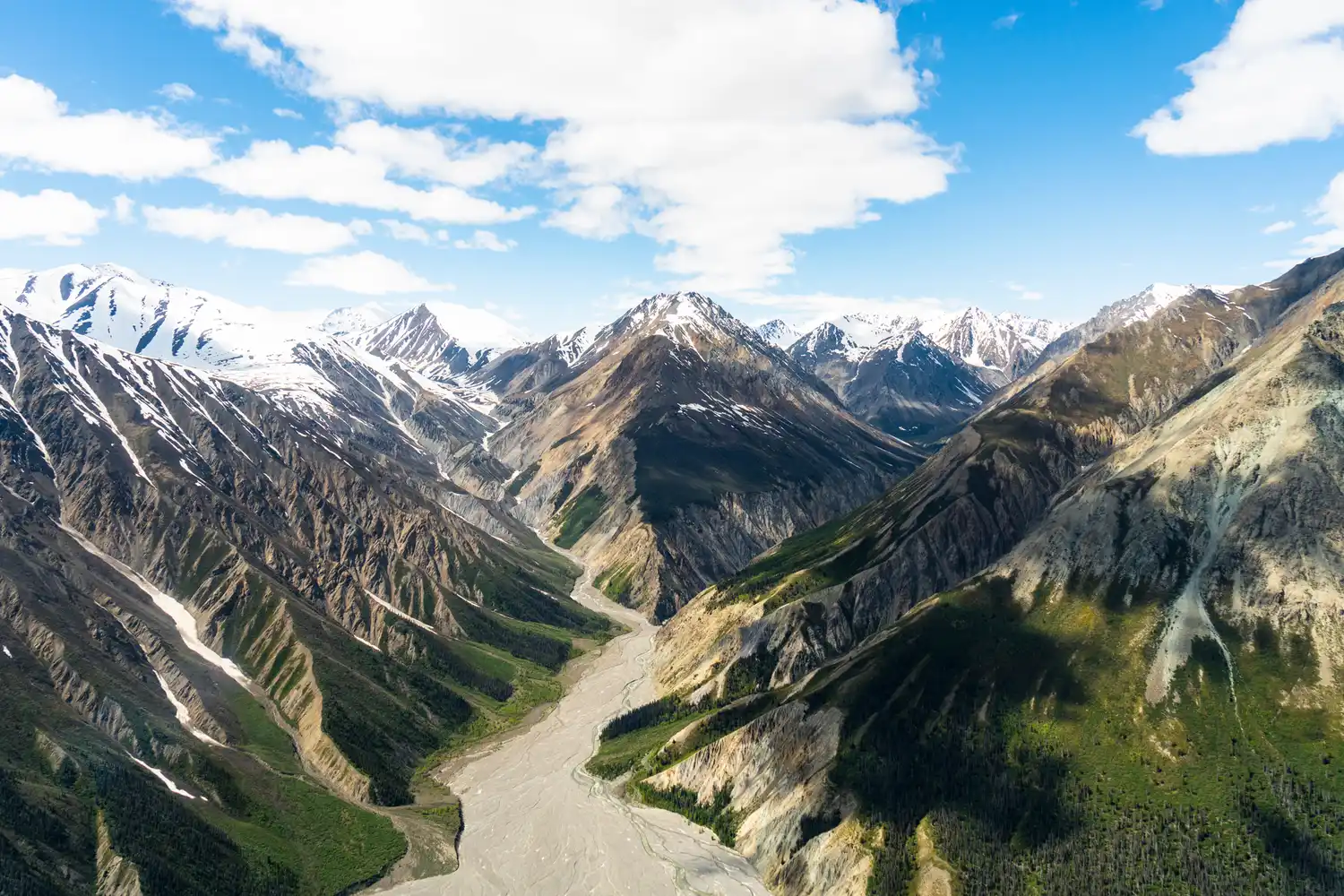 An expansive valley with a braided river system cutting through steep mountain ranges under a cloudy sky.