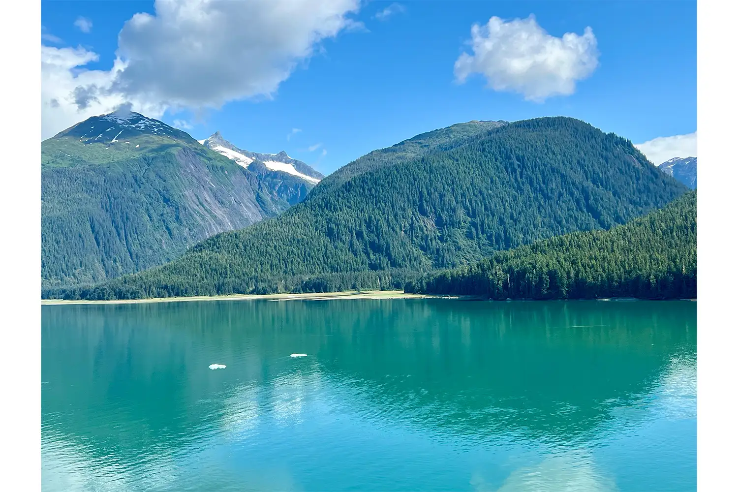 Scenic view of a tranquil lake surrounded by forested mountains under a partially cloudy sky.