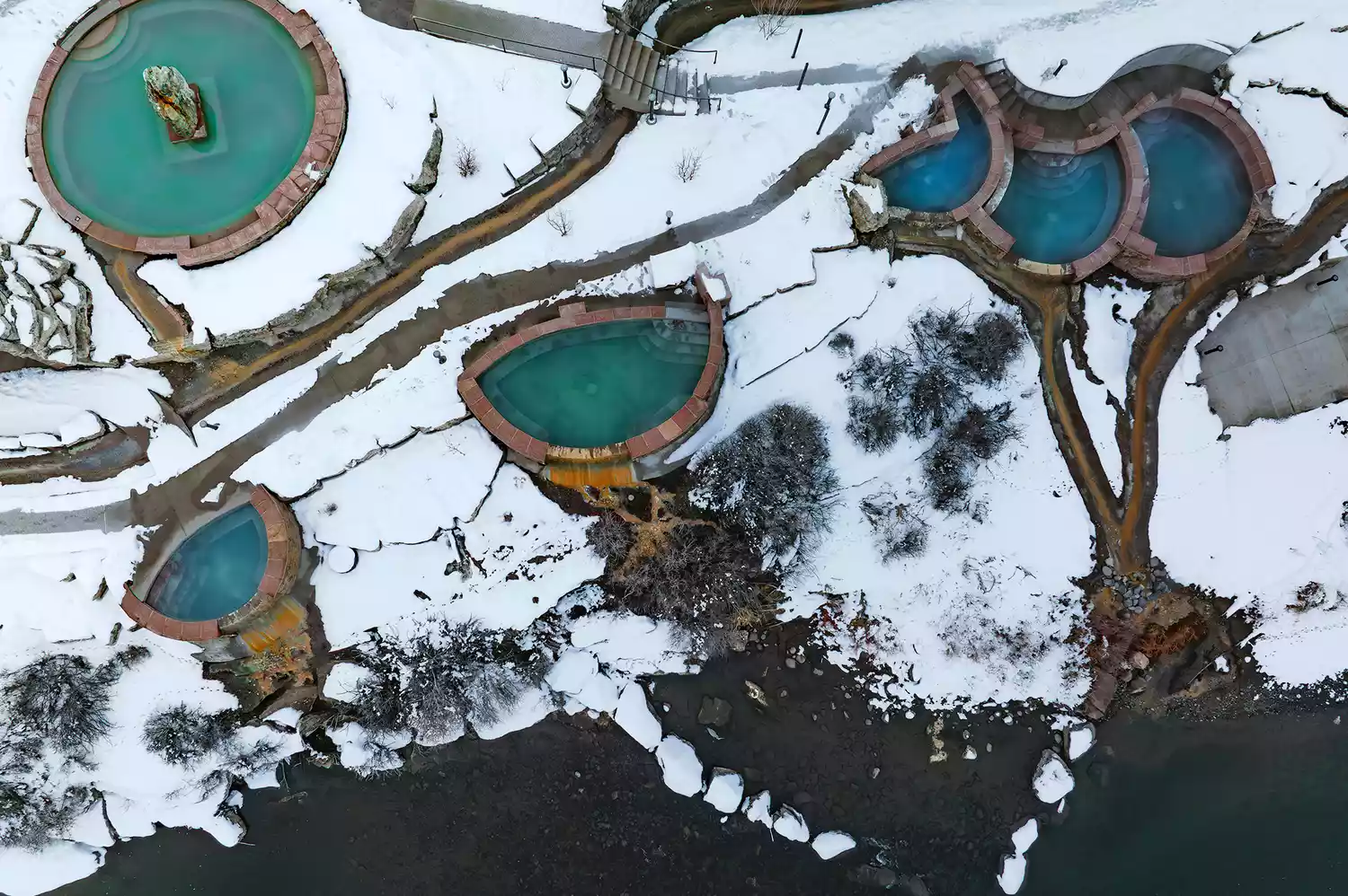 High-angle aerial view of several mineral-rich soaking pools terraced along the banks of the San Juan River.