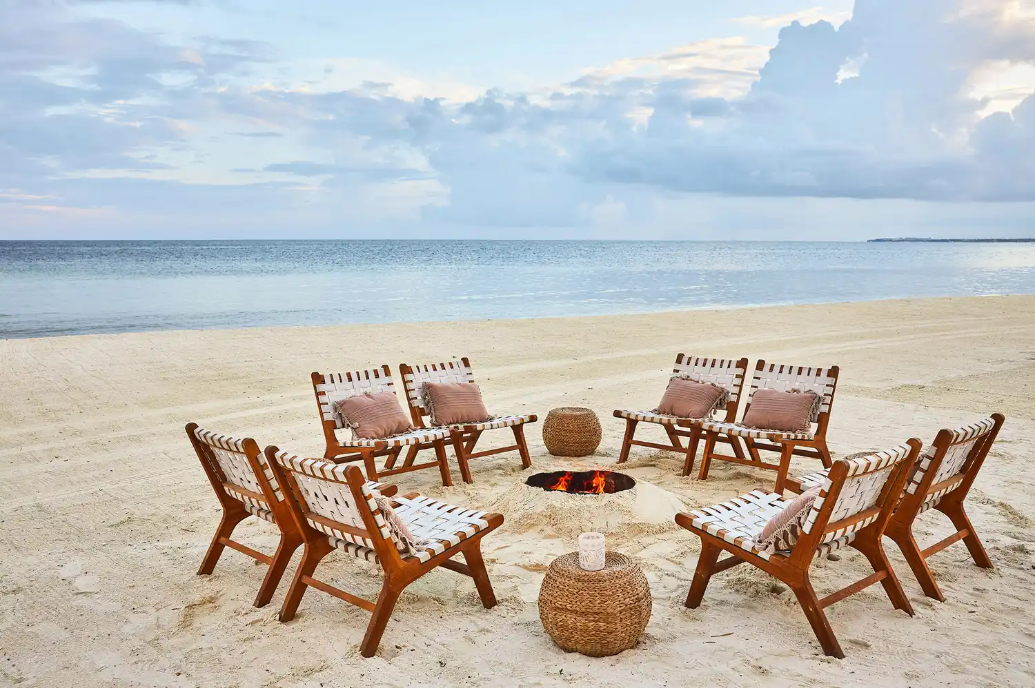 Beach bonfire setup with wooden chairs on sand under a twilight sky.