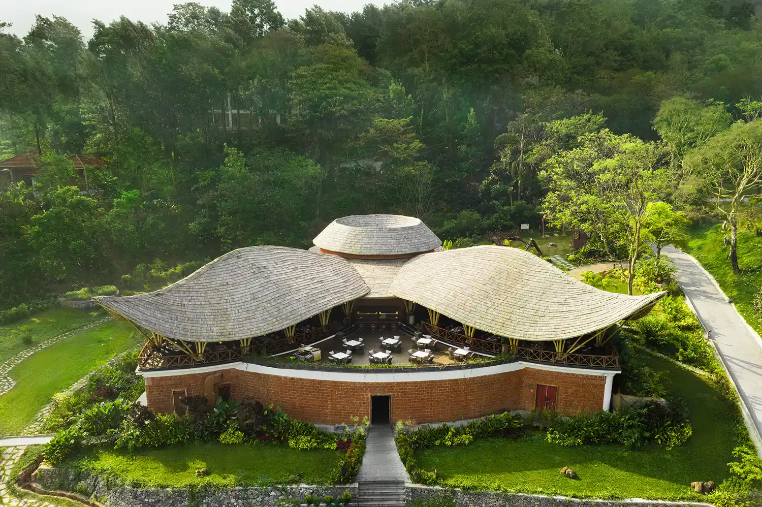 An open-air thatched roof pavilion restaurant surrounded by lush greenery and manicured gardens.