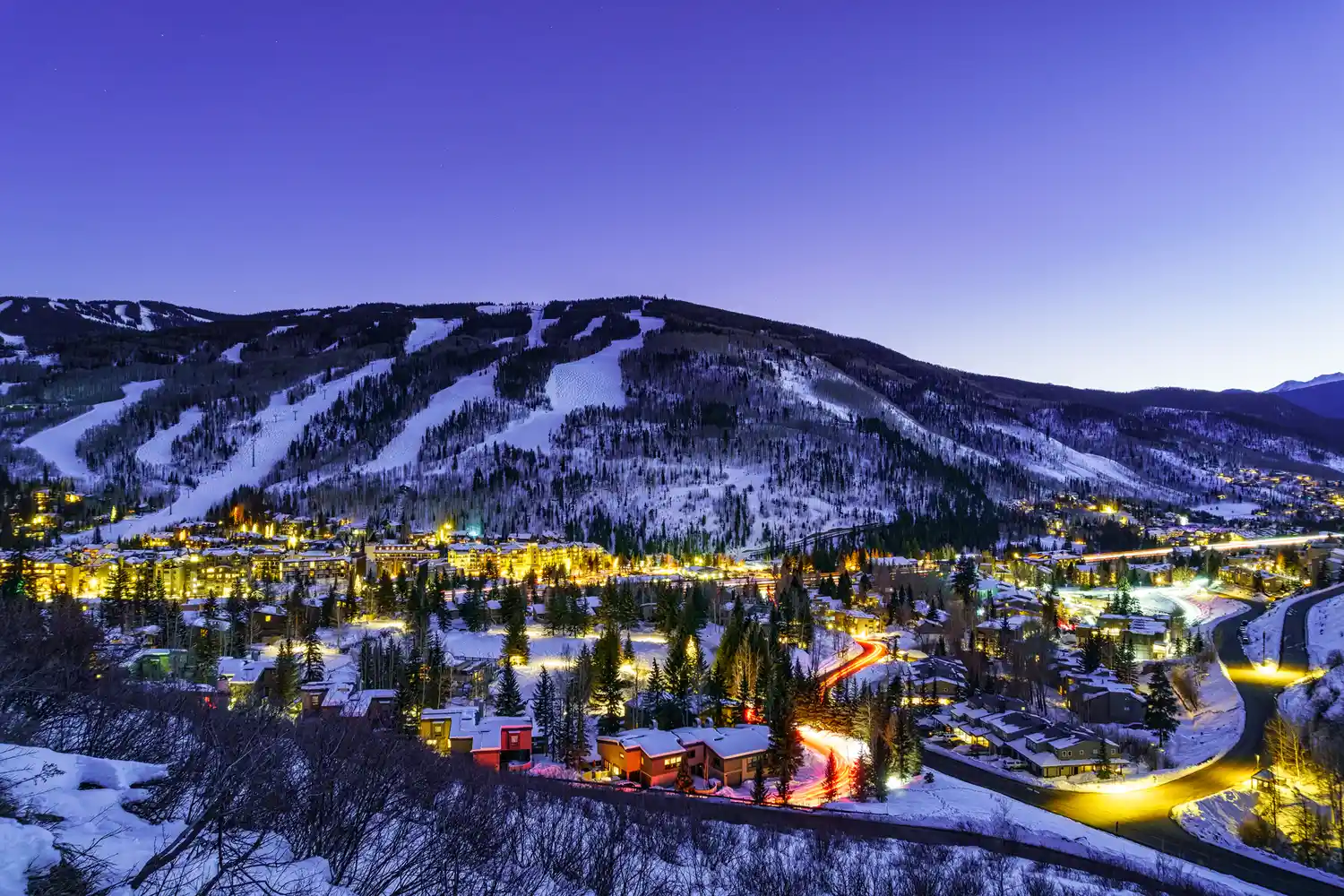 Aerial twilight view of the lit-up Vail Village surrounded by snowy mountains.