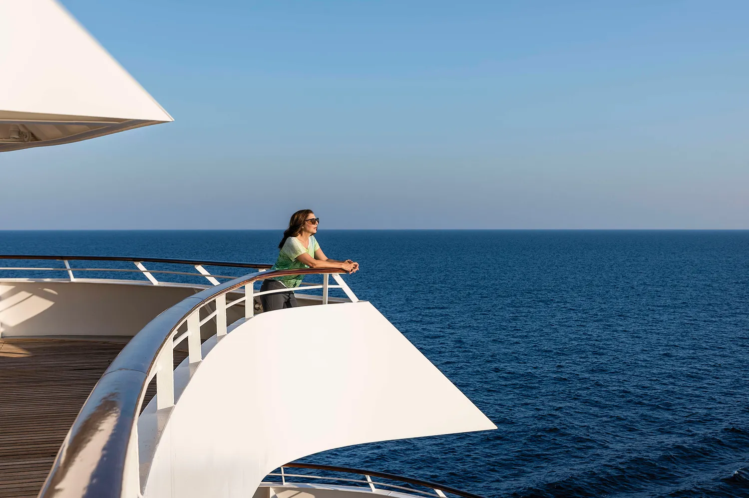 A woman traveler standing on a cruise ship deck looking out at the ocean horizon.