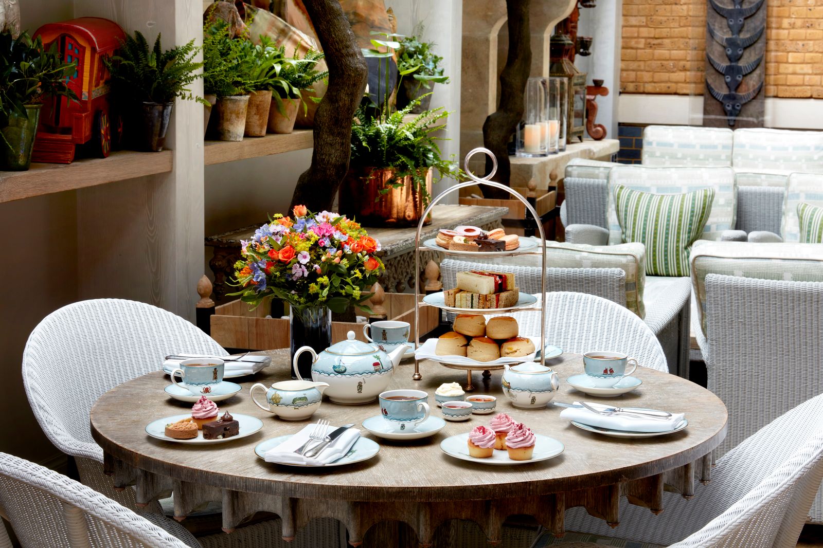 A beautifully set brunch table with coffee, pastries, and plants in a brightly lit dining room.