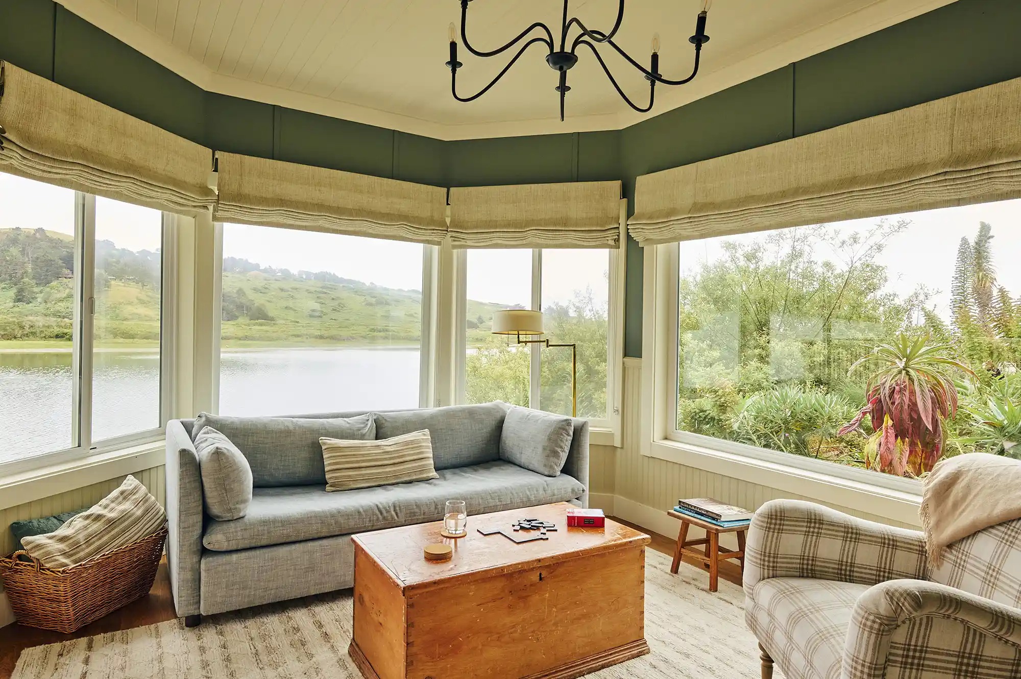 A cozy living area featuring a plaid armchair, a wooden chest coffee table, and large windows inviting natural light.