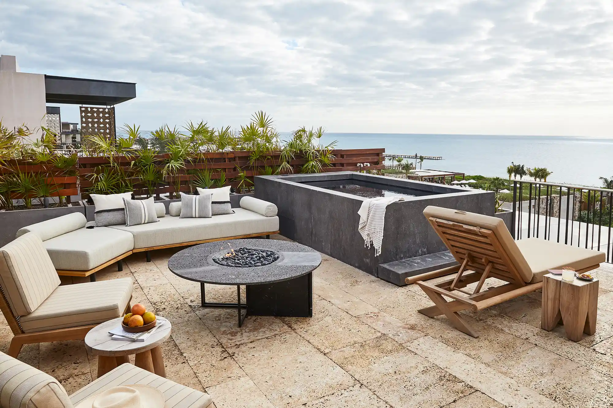 A luxury outdoor terrace with a private plunge pool, fire pit, and lounge seating overlooking the ocean.
