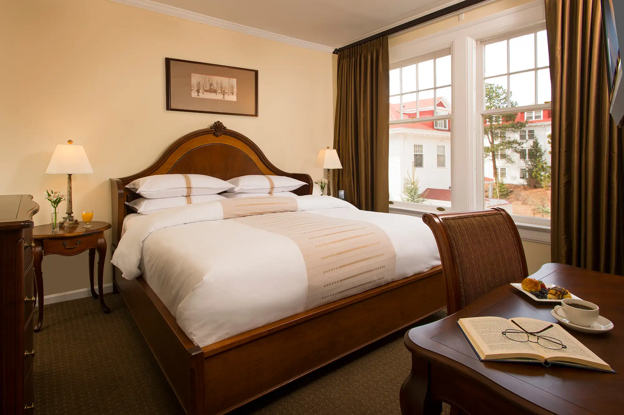A historic hotel room featuring a traditional wooden desk with a notebook and a view of a red-roofed building through the window.