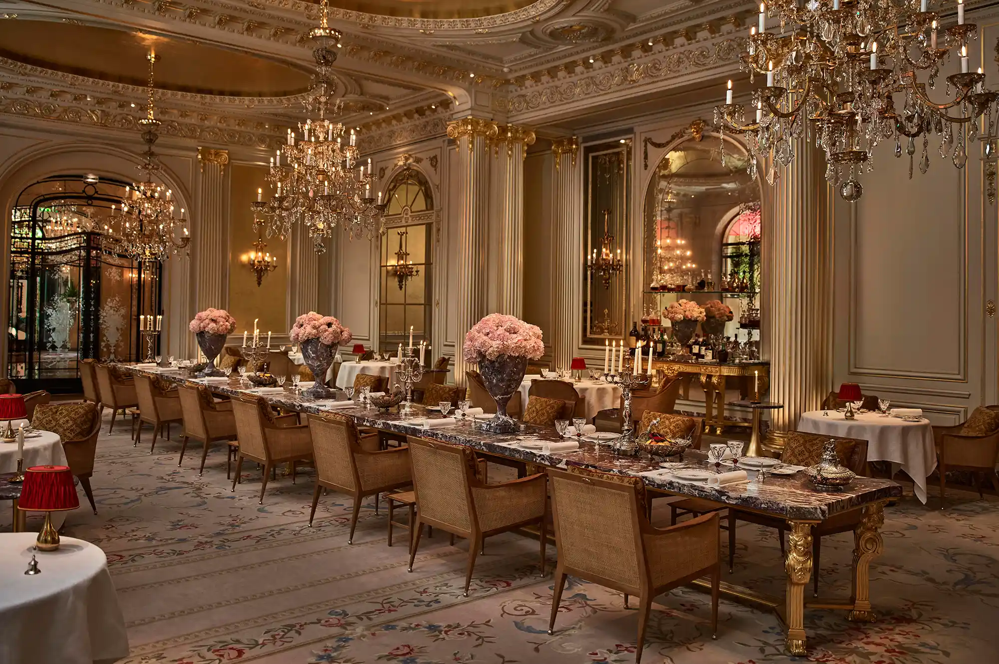 Grand dining room with intricate chandeliers, floral arrangements, and gold-accented architecture.