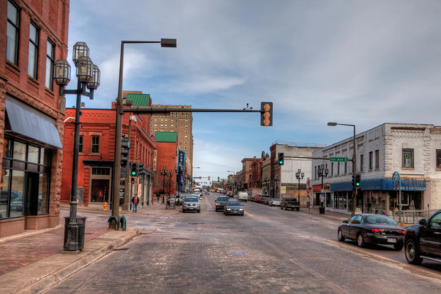 A street view of downtown Duluth showing the hilly terrain, historic buildings, and traffic during the day.