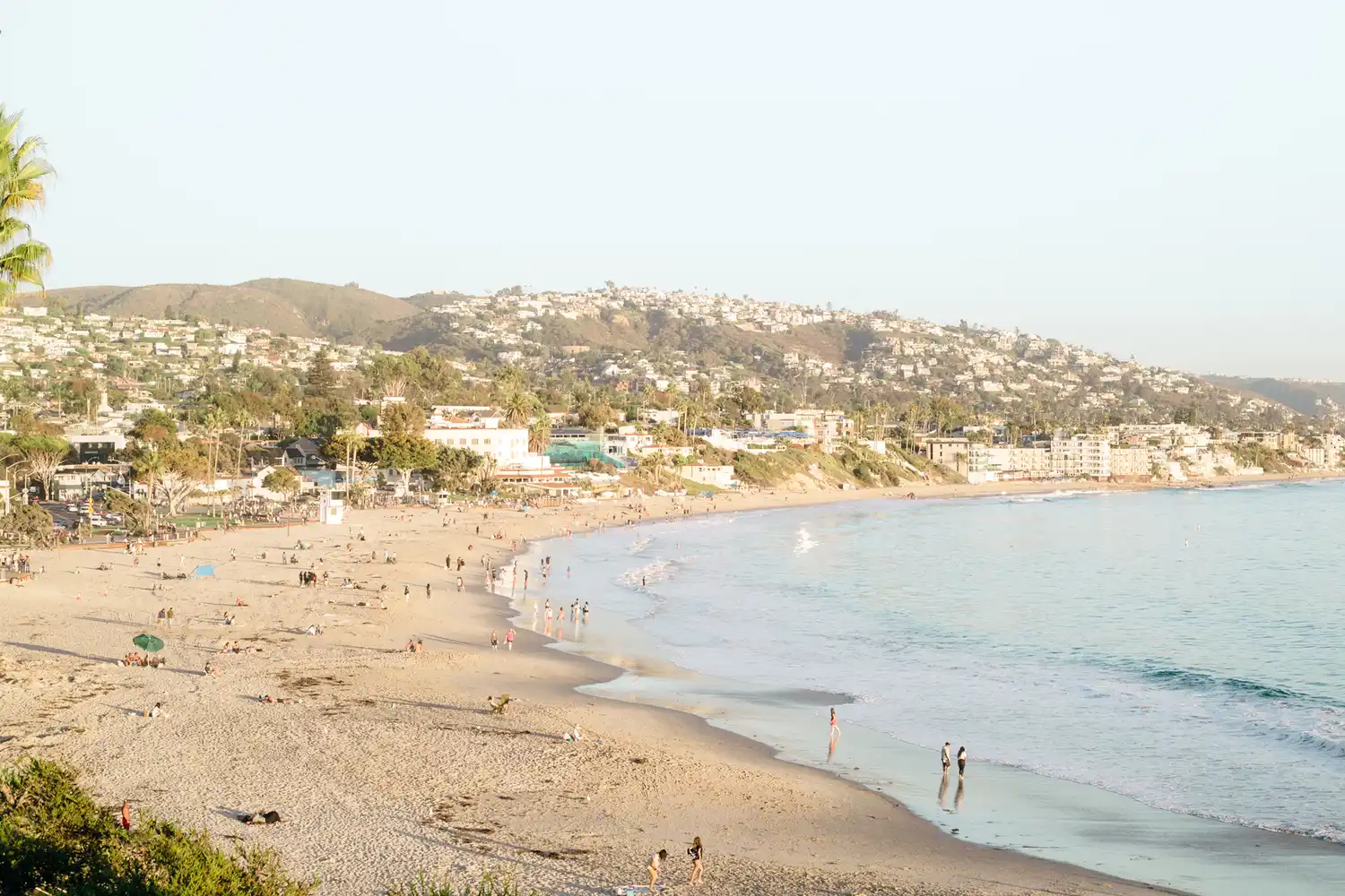 Wide shot of sandy beaches and crystal clear water adjacent to green coastal hills.