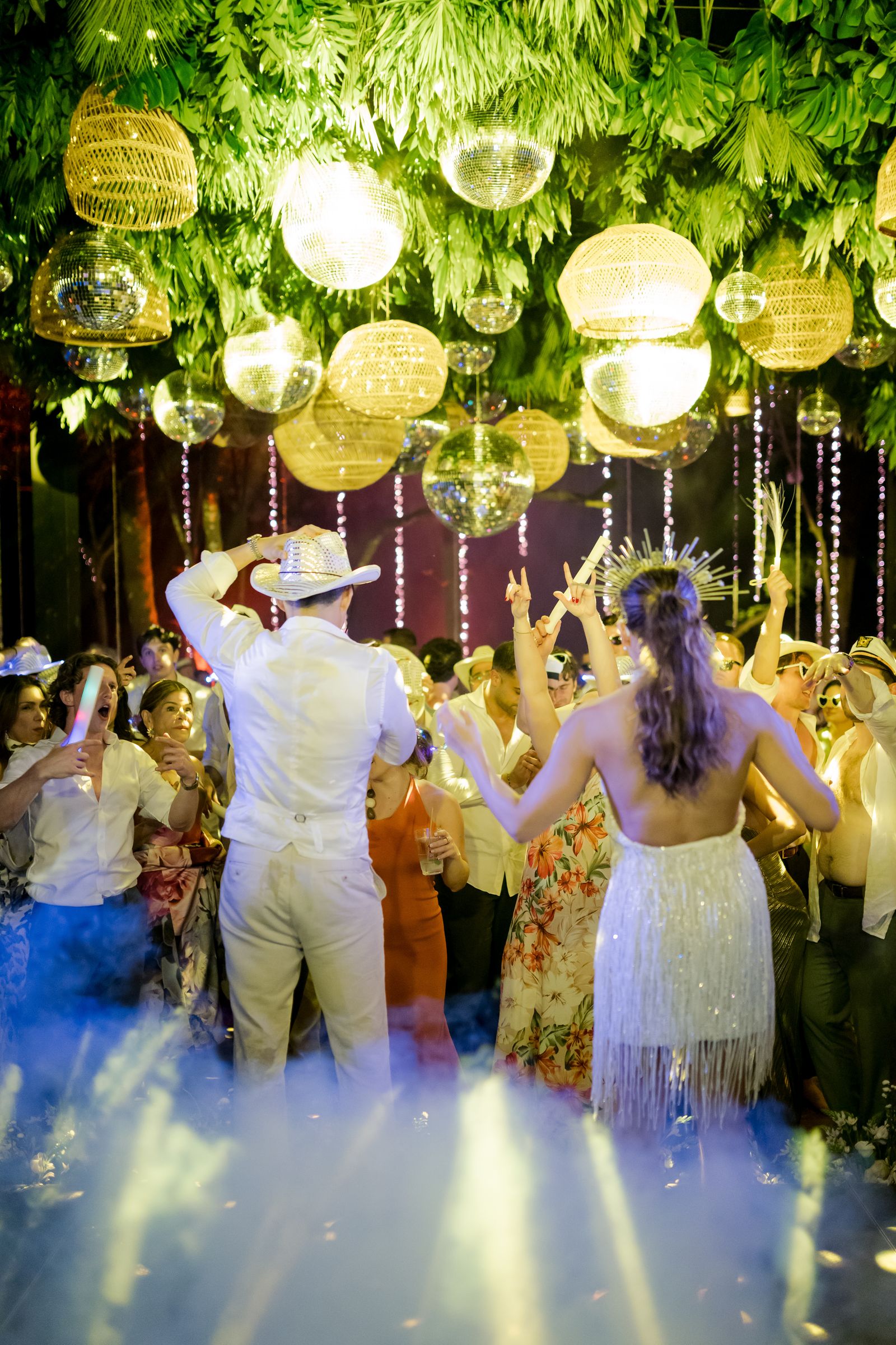 People celebrating and dancing at a wedding party with festive lighting.