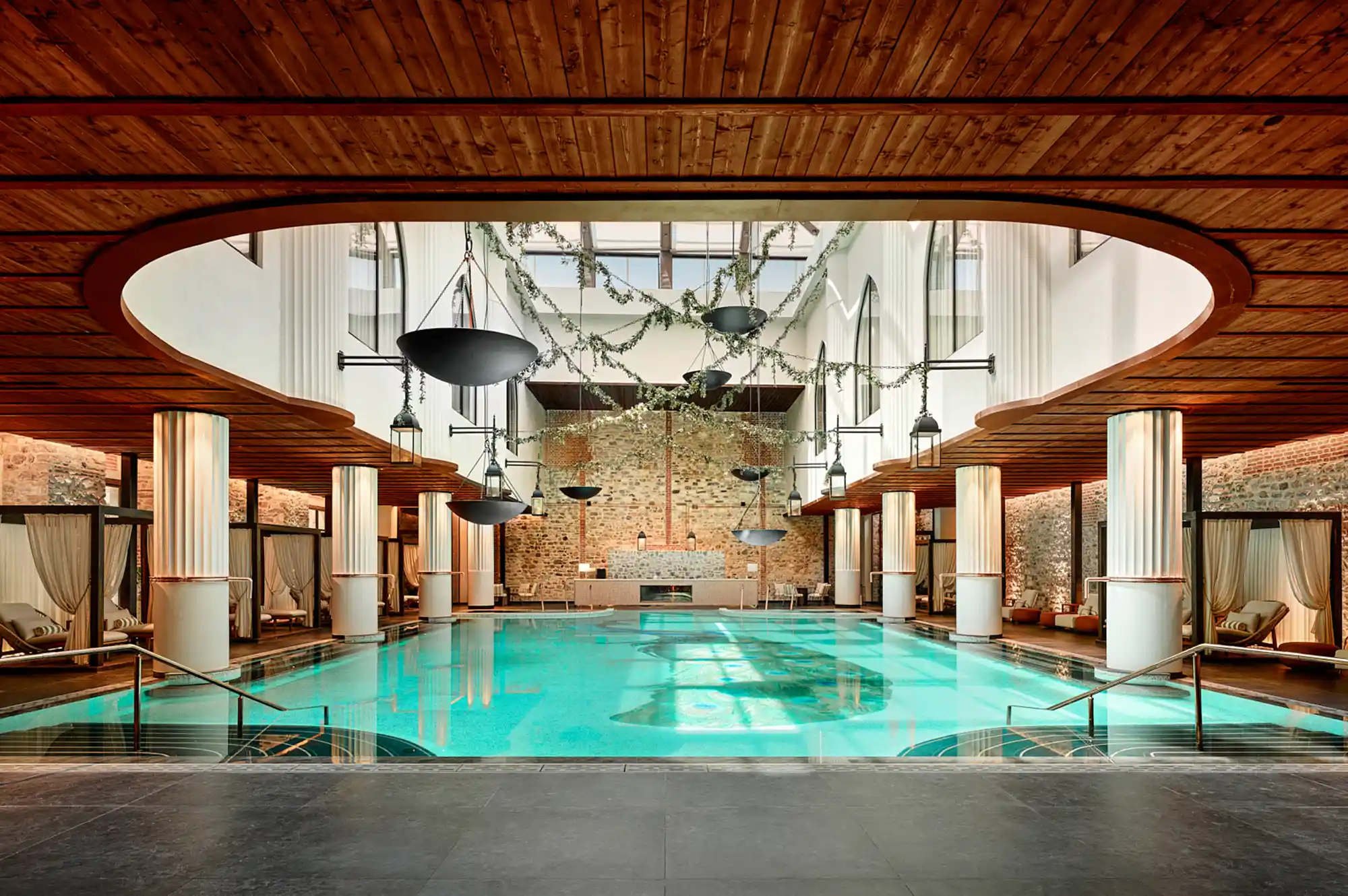 Indoor infinity pool area with warm wood-paneled ceilings and ambient lighting in the spa complex.