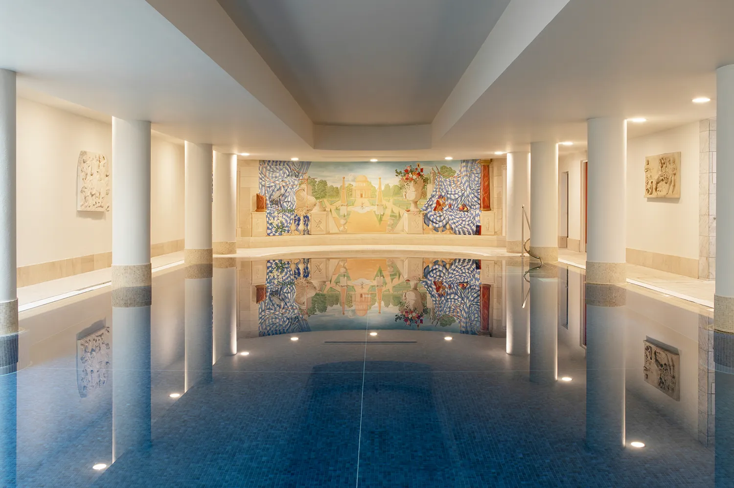 An expansive indoor infinity swimming pool lined with pillars and a decorative mural.