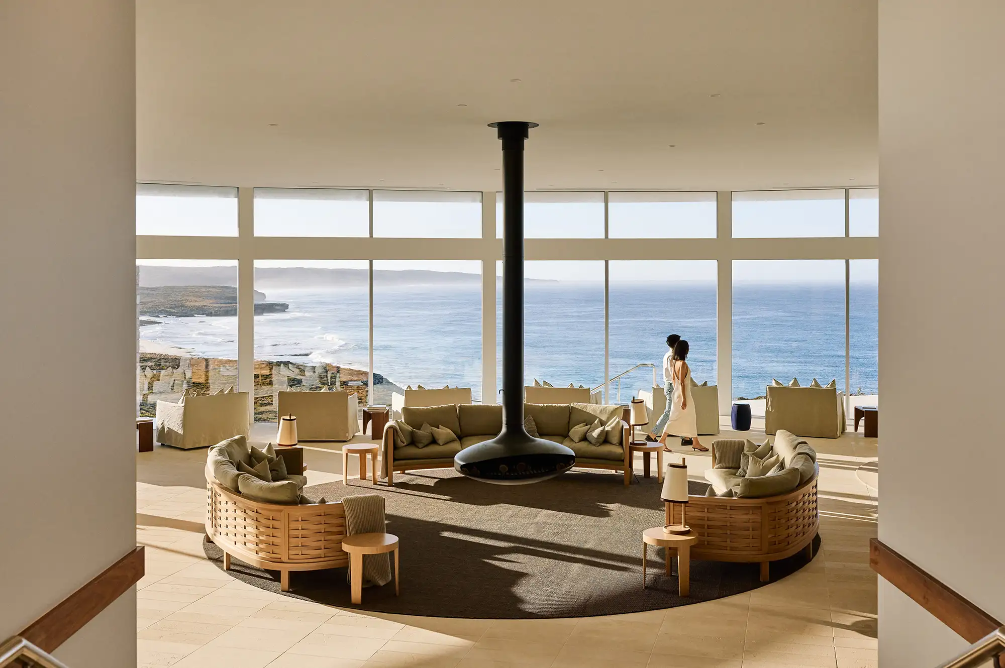 Modern lounge with a suspended fireplace and large glass windows viewing the rugged ocean coast.