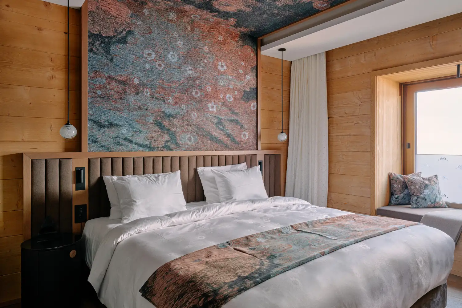 A guest room at Huus Quell in Switzerland with warm wooden walls and floral decor.