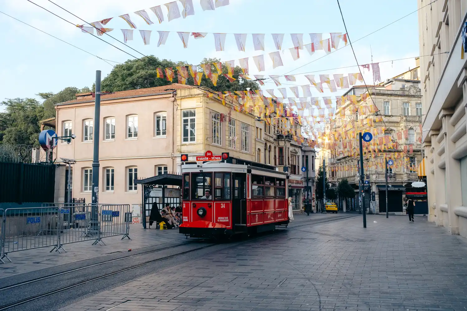 A red historic tram car traveling through the busy, flag-lined streets of Beyoğlu.