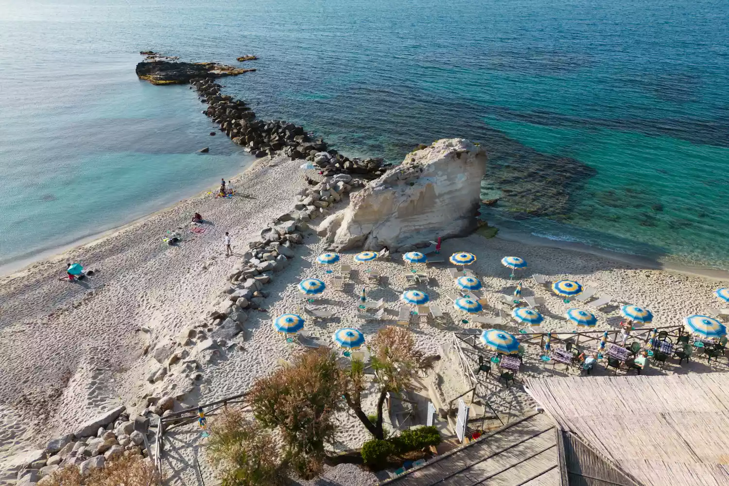 Aerial drone view of beach umbrellas and people on the sandy shore of Tropea with turquoise water.