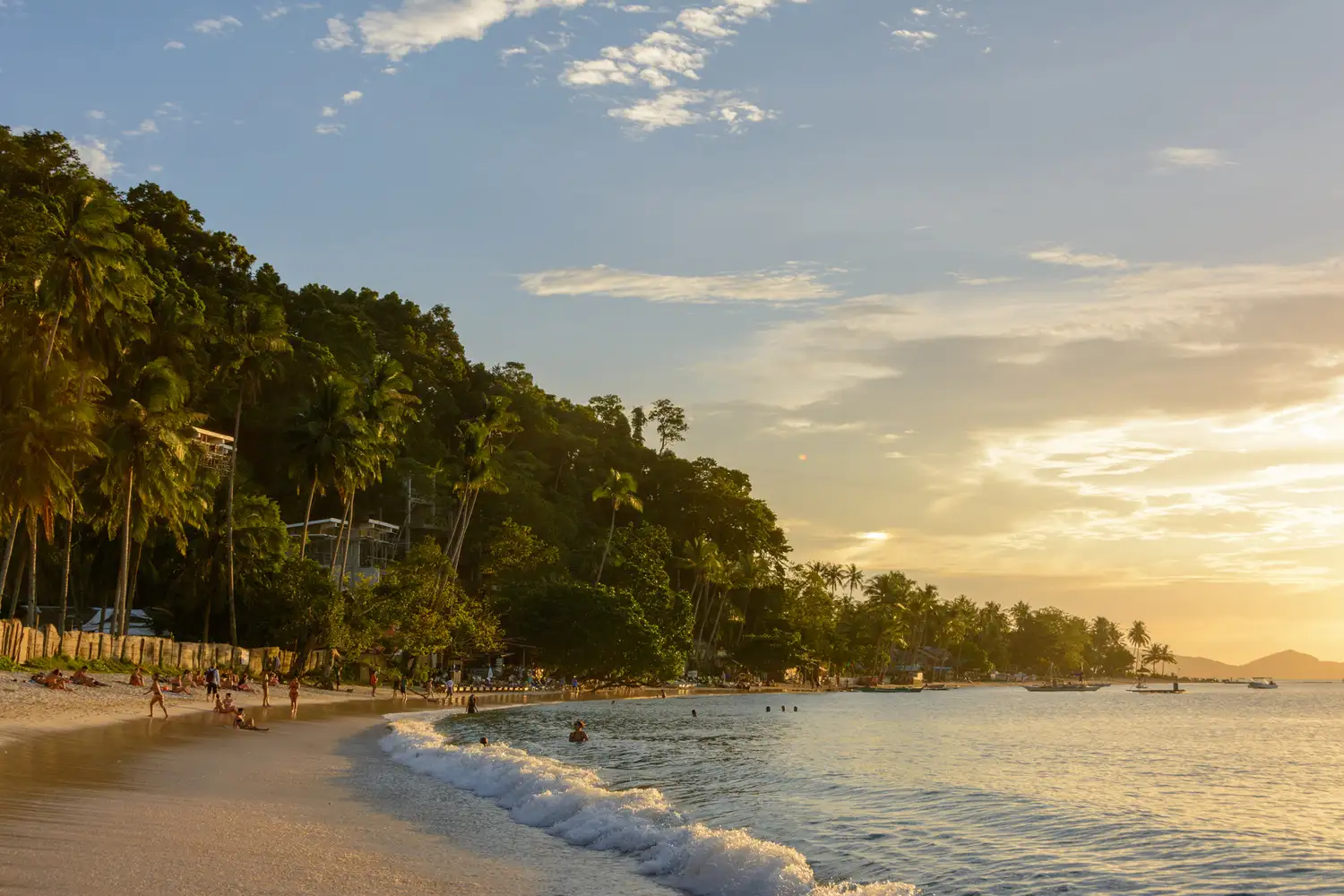 Sunset over a tropical beach in Palawan with palm trees in the foreground.