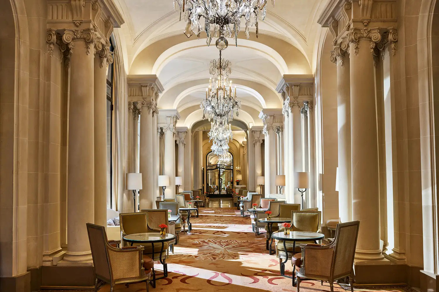 A long, elegant hallway with columns and plush seating under grand chandeliers.