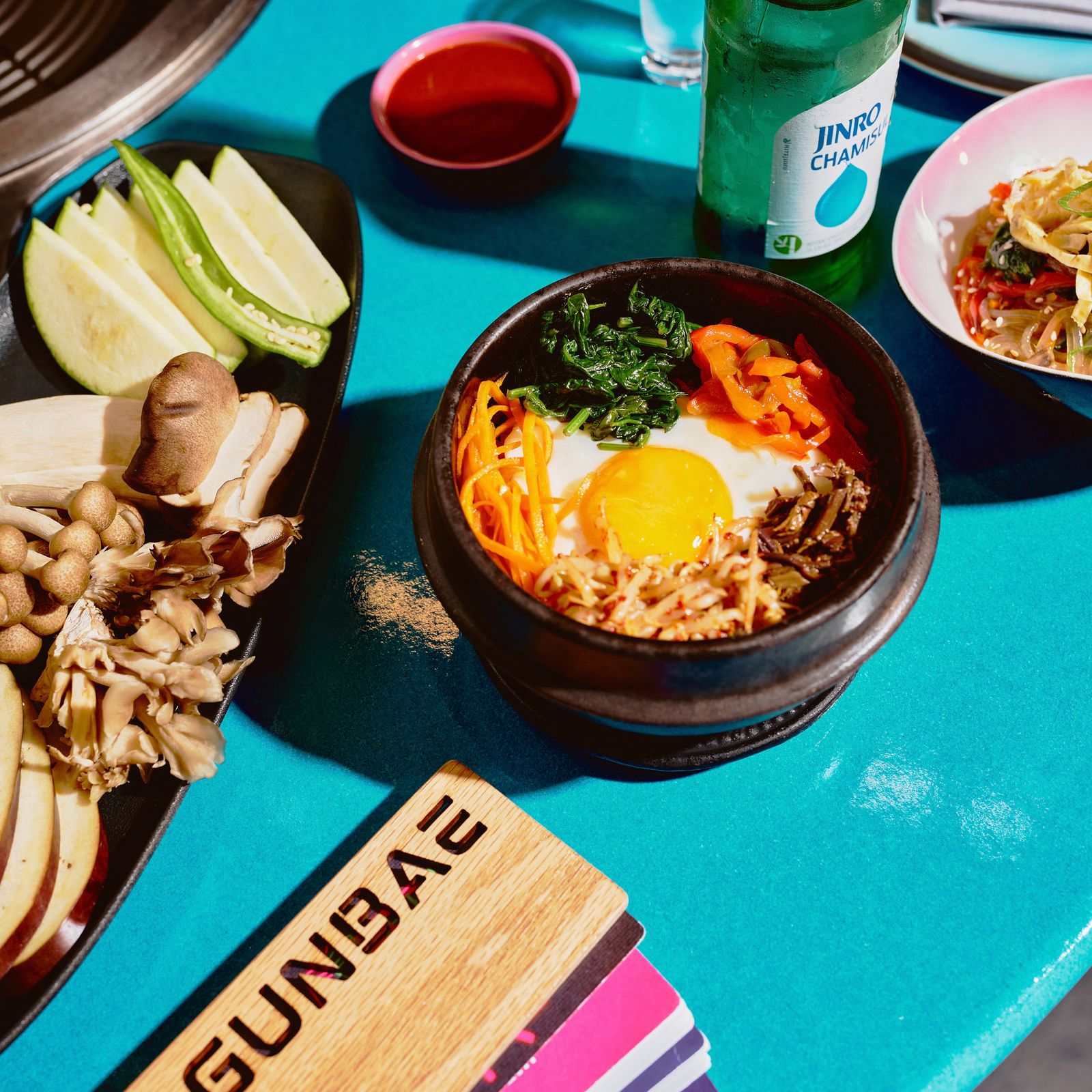 A colorful spread of Korean BBQ dishes including eggs, bowls of various sides, and communal dining items.