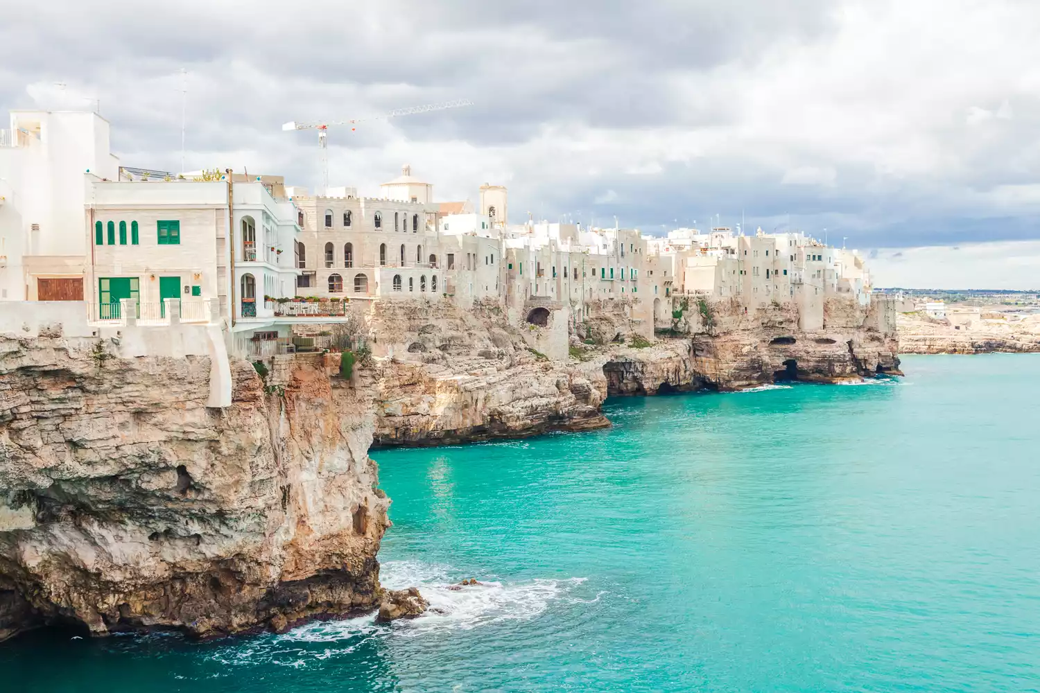 Antique buildings of Polignano a Mare perched on a rocky cliff above the blue Adriatic Sea.