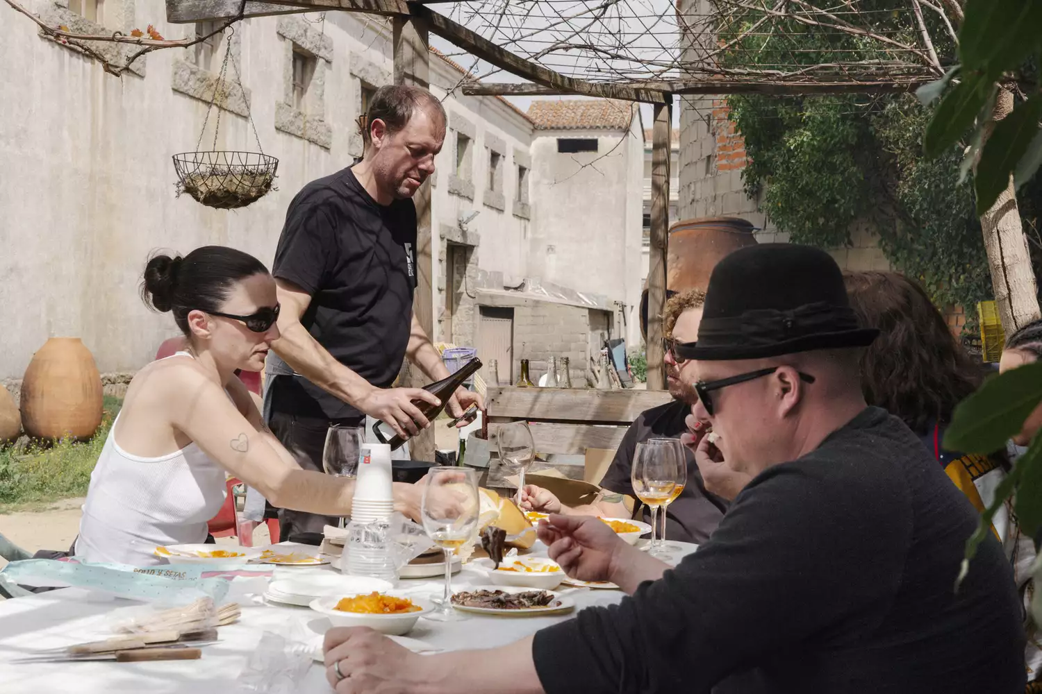 A group of people sitting at a long outdoor table sharing a meal in the middle of a vineyard.