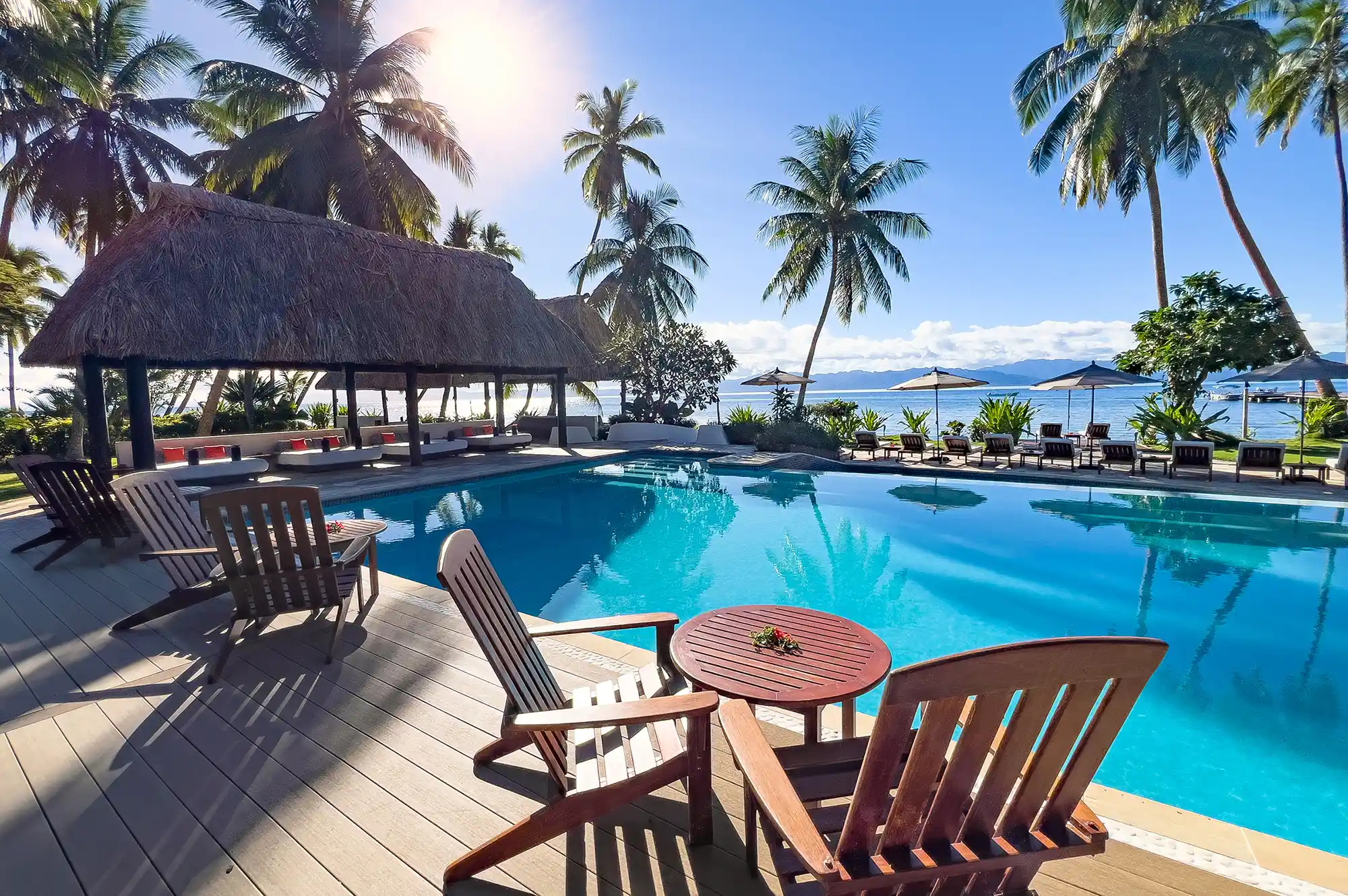 A scenic tropical resort pool area with lounge chairs and palm trees overlooking the ocean.