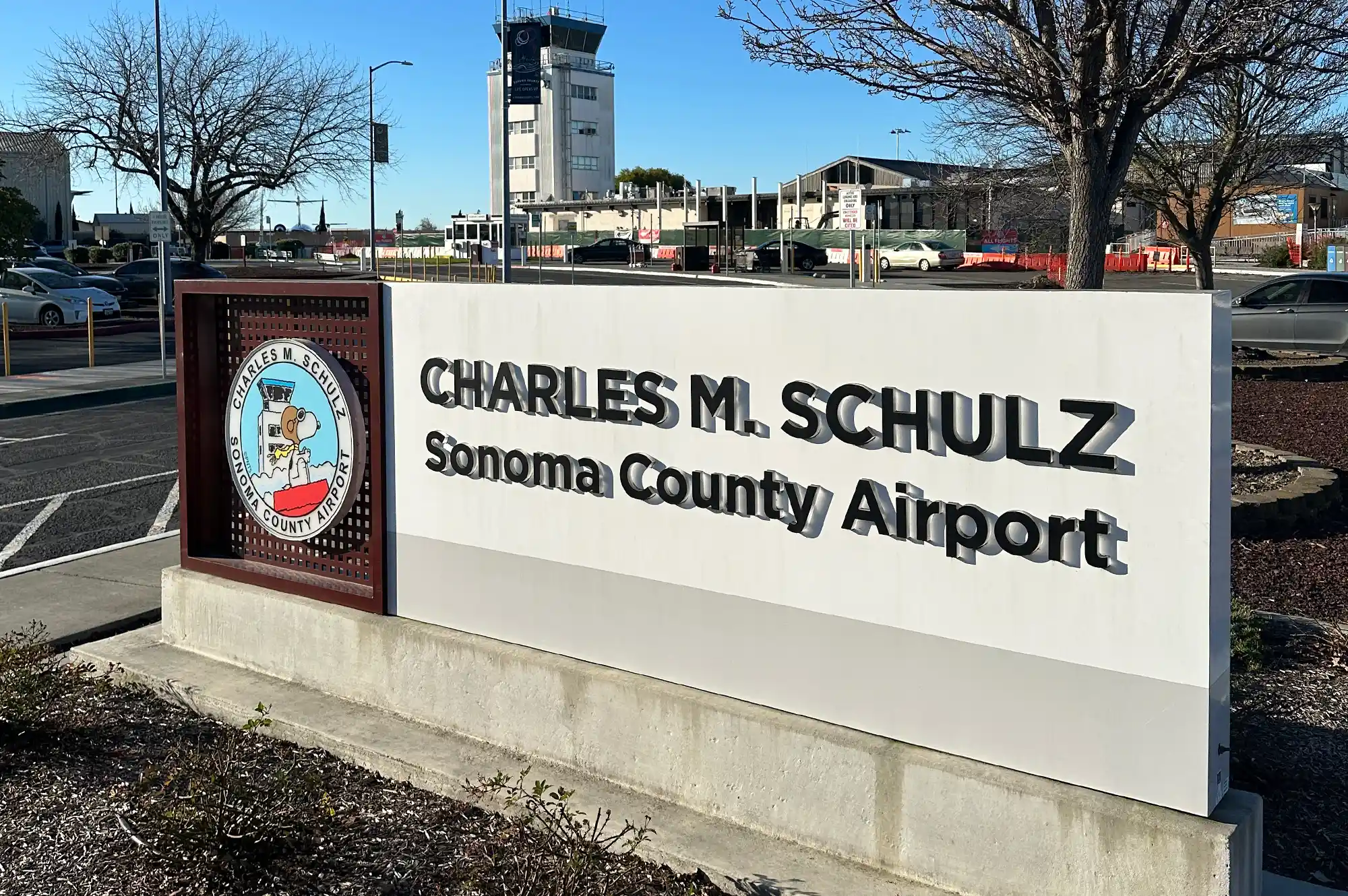The roadside sign for Charles M. Schulz Sonoma County Airport with the control tower in the background.