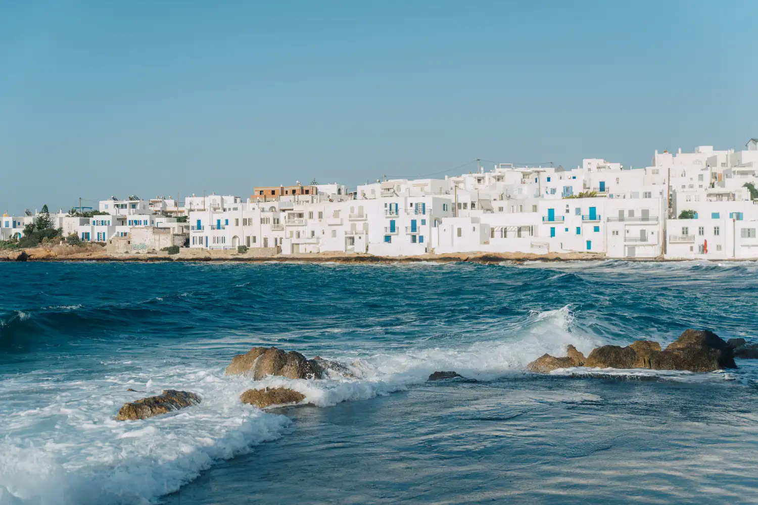 White buildings and stone walls along the turquoise coastline of Paros, Greece.
