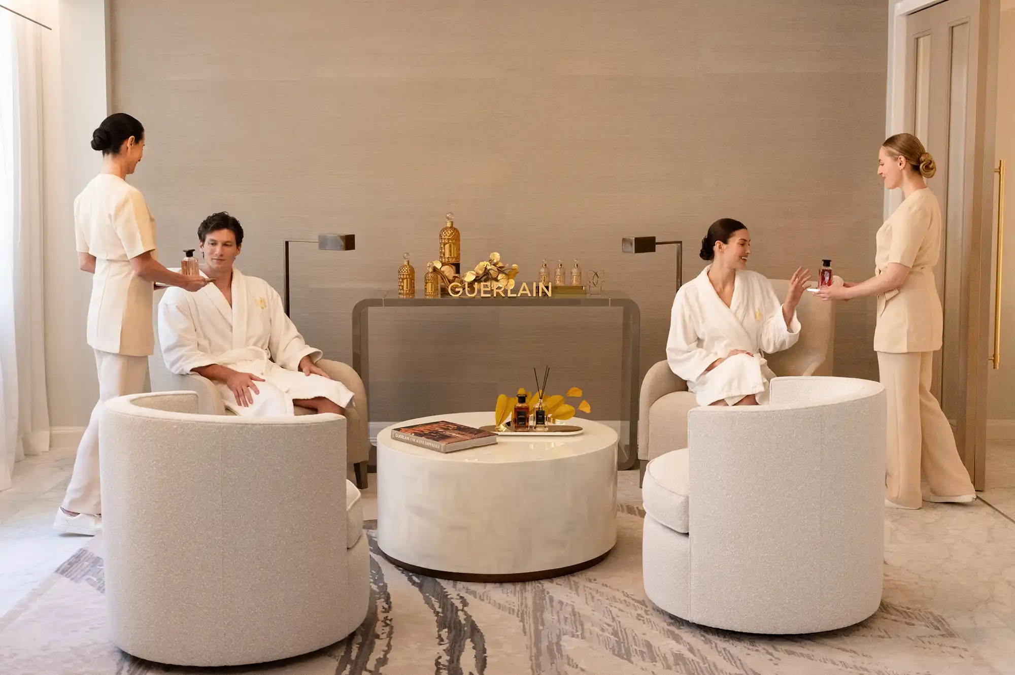 Guests in white robes relaxing in a brightly lit, modern wellness lounge at the Guerlain Spa.