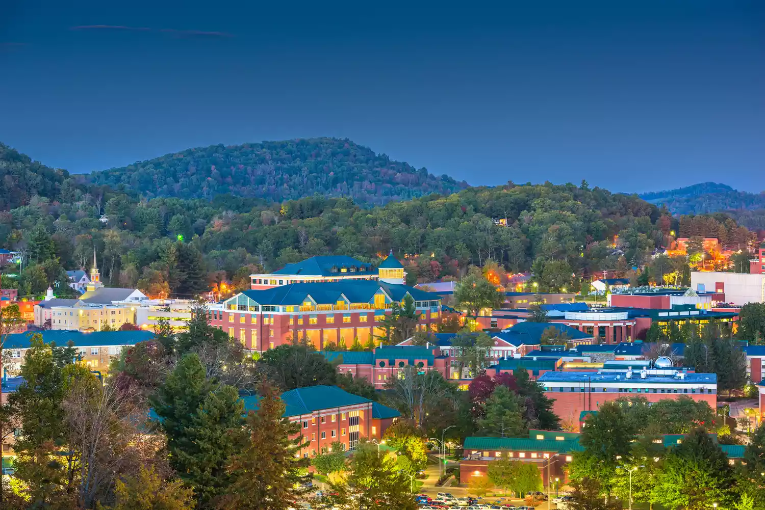 Aerial nighttime view of downtown Boone with city lights and mountain backdrop.