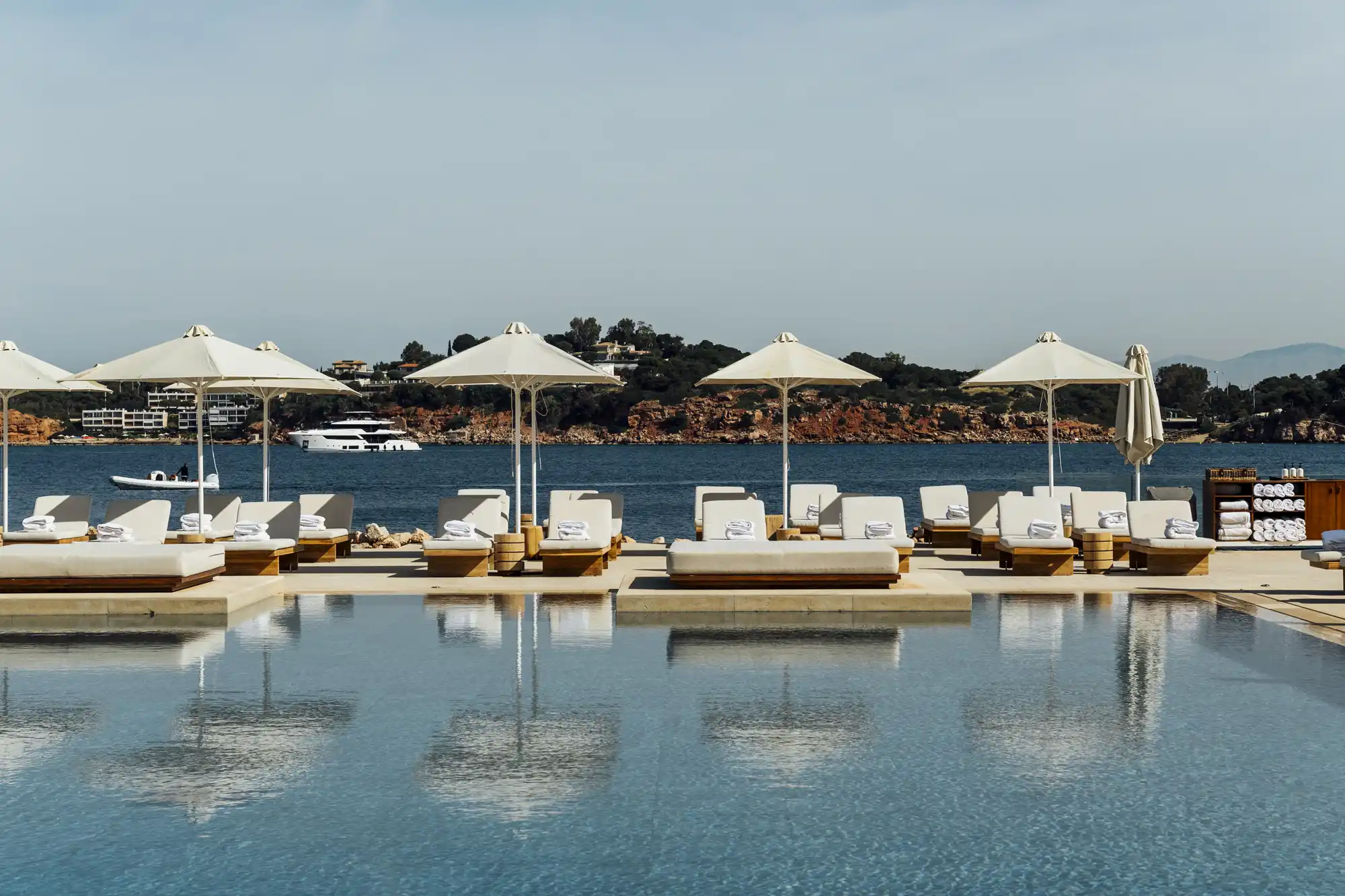A luxury infinity pool at an Athenian resort overlooking the blue waters of the Saronic Gulf with white umbrellas.