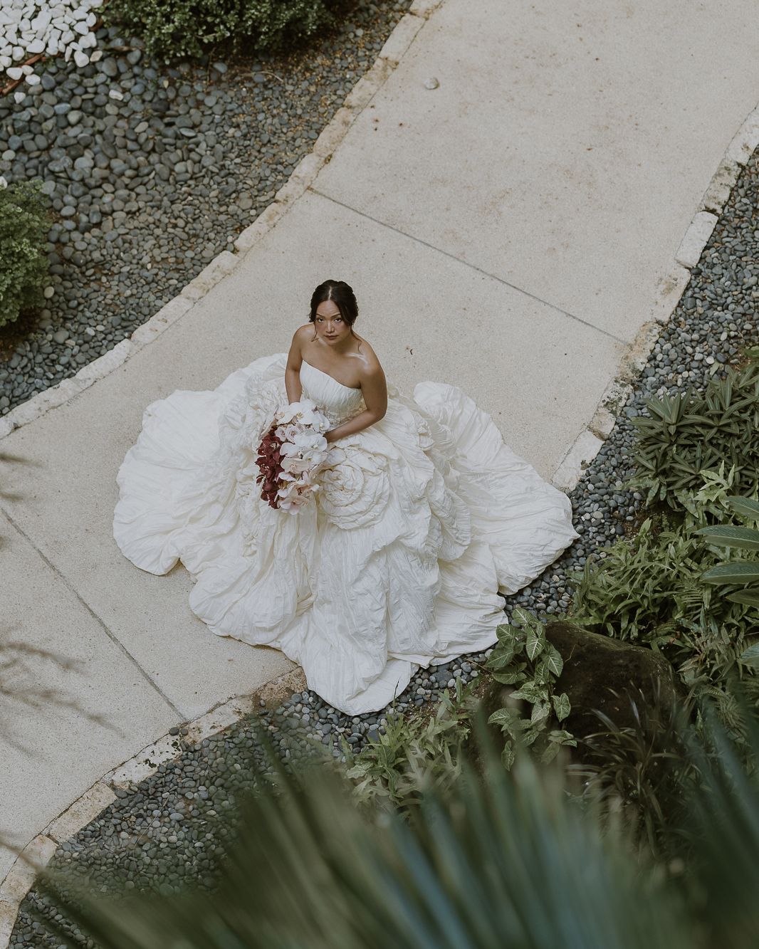 A bride in a modern Filipiniana-inspired wedding gown walking down a sunlit outdoor path.