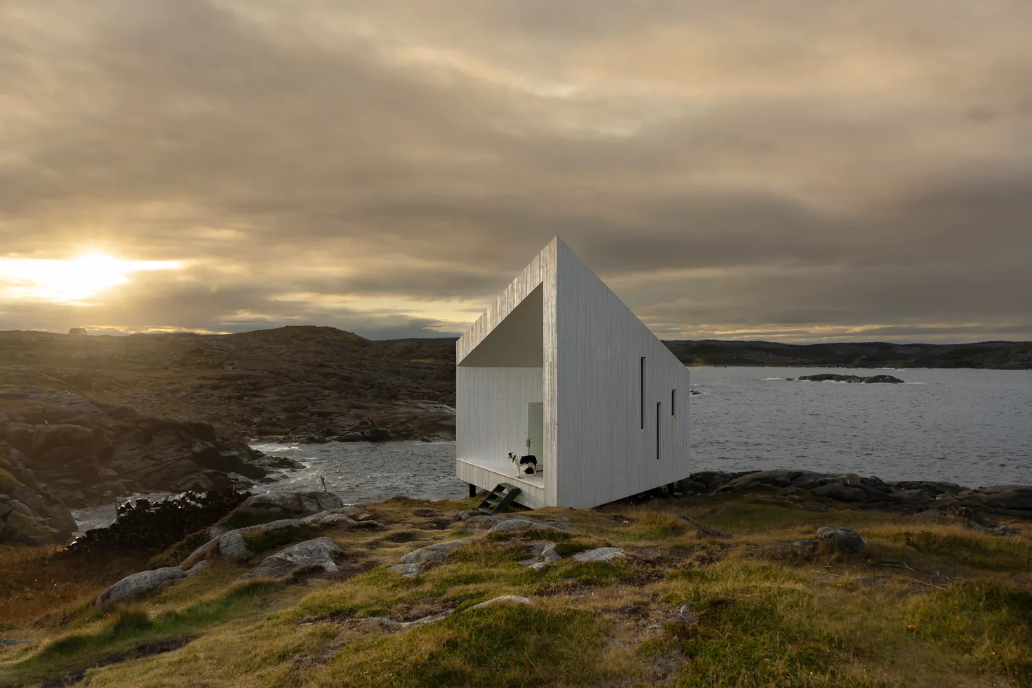 The Squish Studio, a geometric white building perched on dark rocks at sunset.