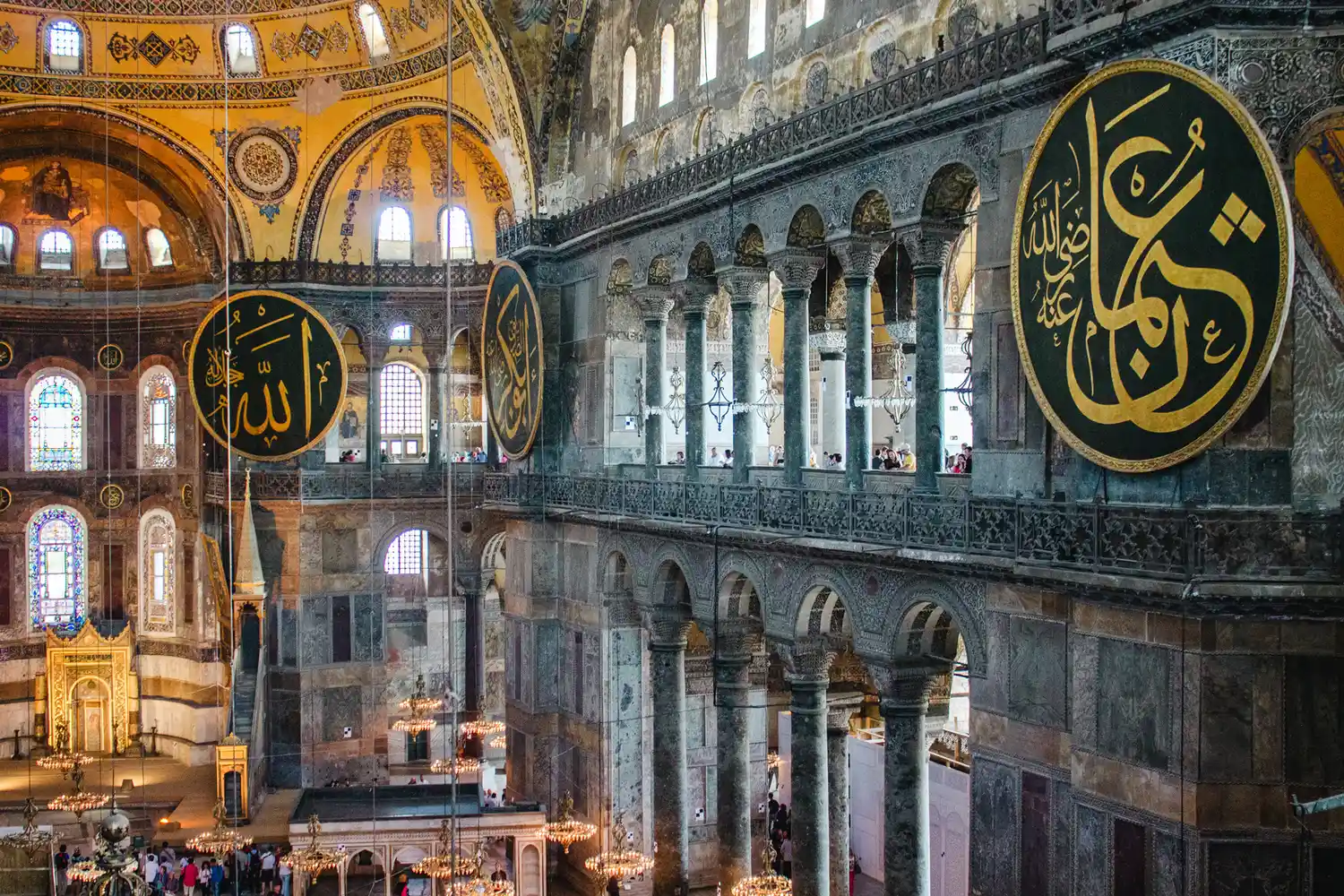The grand interior of Hagia Sophia featuring Islamic calligraphy medallions and golden mosaics.