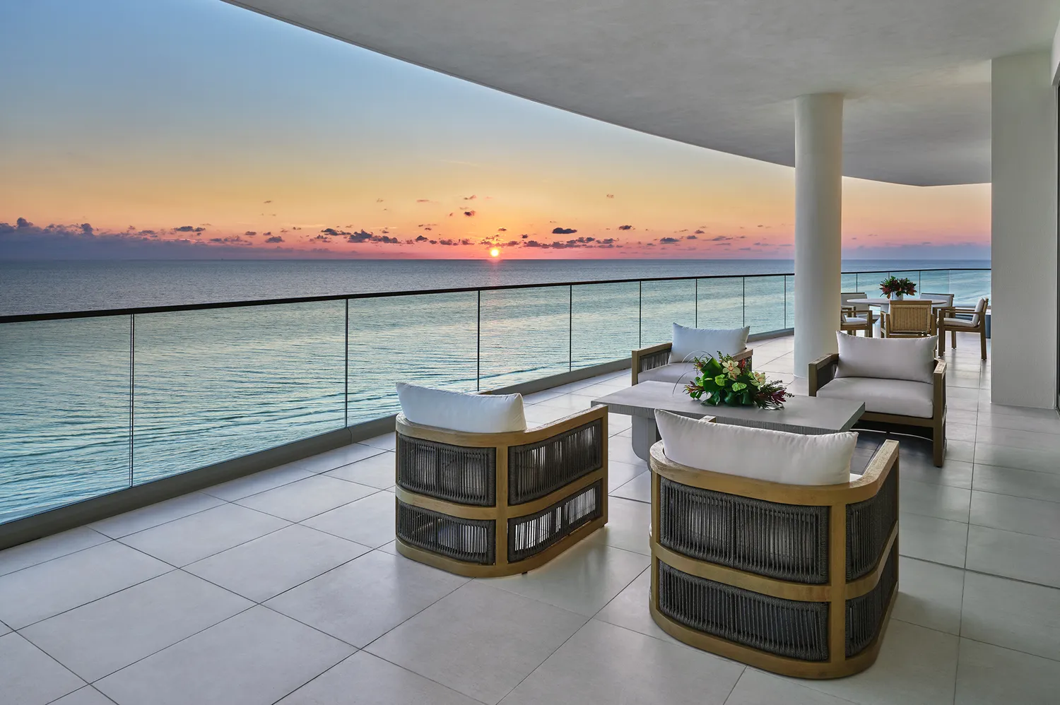 An expansive outdoor terrace with modern furniture overlooking the Gulf of Mexico during a sunset.