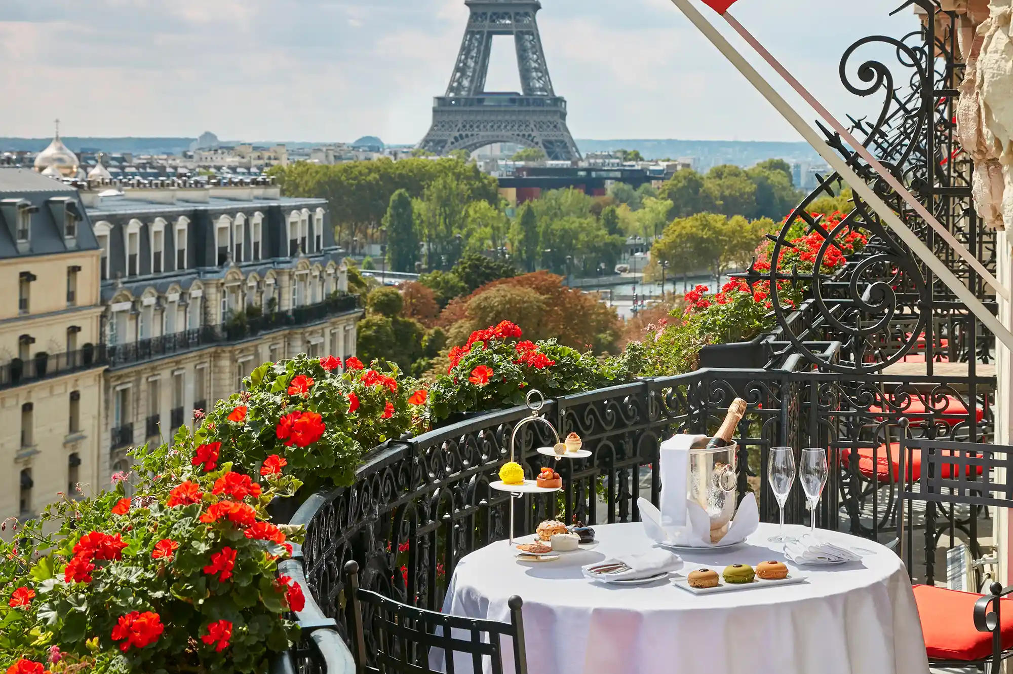 A private balcony set with white linens and breakfast items overlooking the Eiffel Tower and Parisian rooftops.